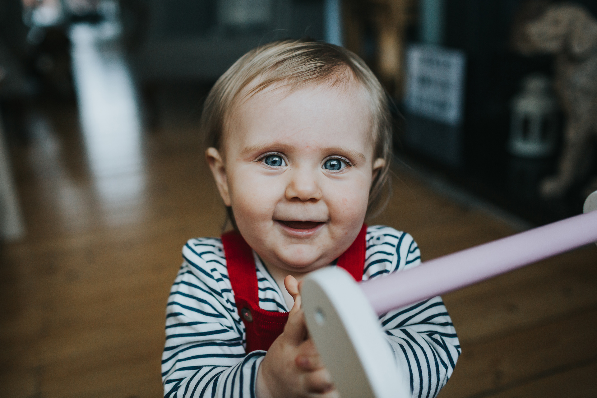One year old girl smile at the camera clasping her hands together in her living room, Merseyside.