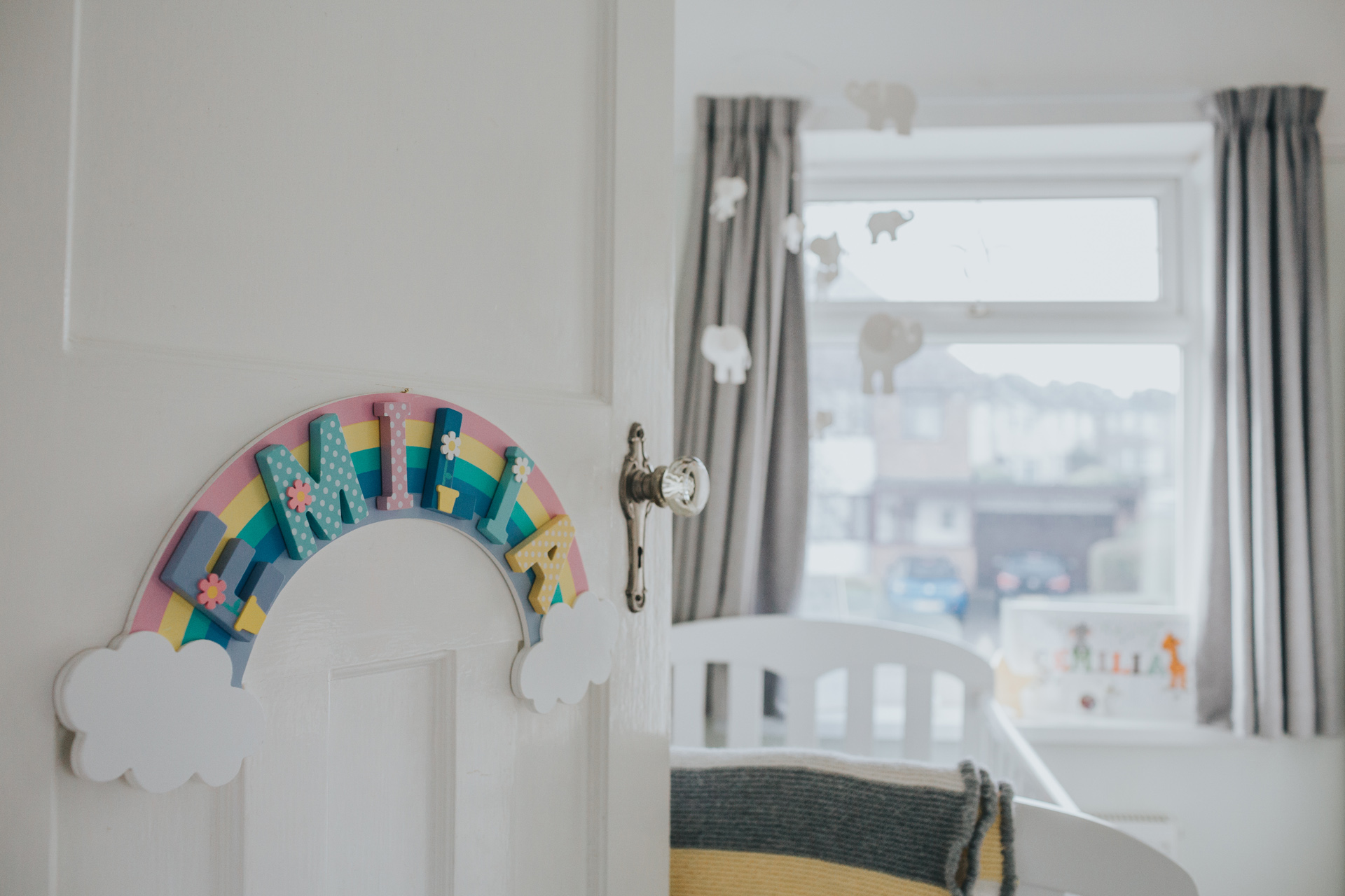 Door with a rainbow sign and Emilia written on it. Beyond the  door we can see a cot and more thoughtful decoration. 