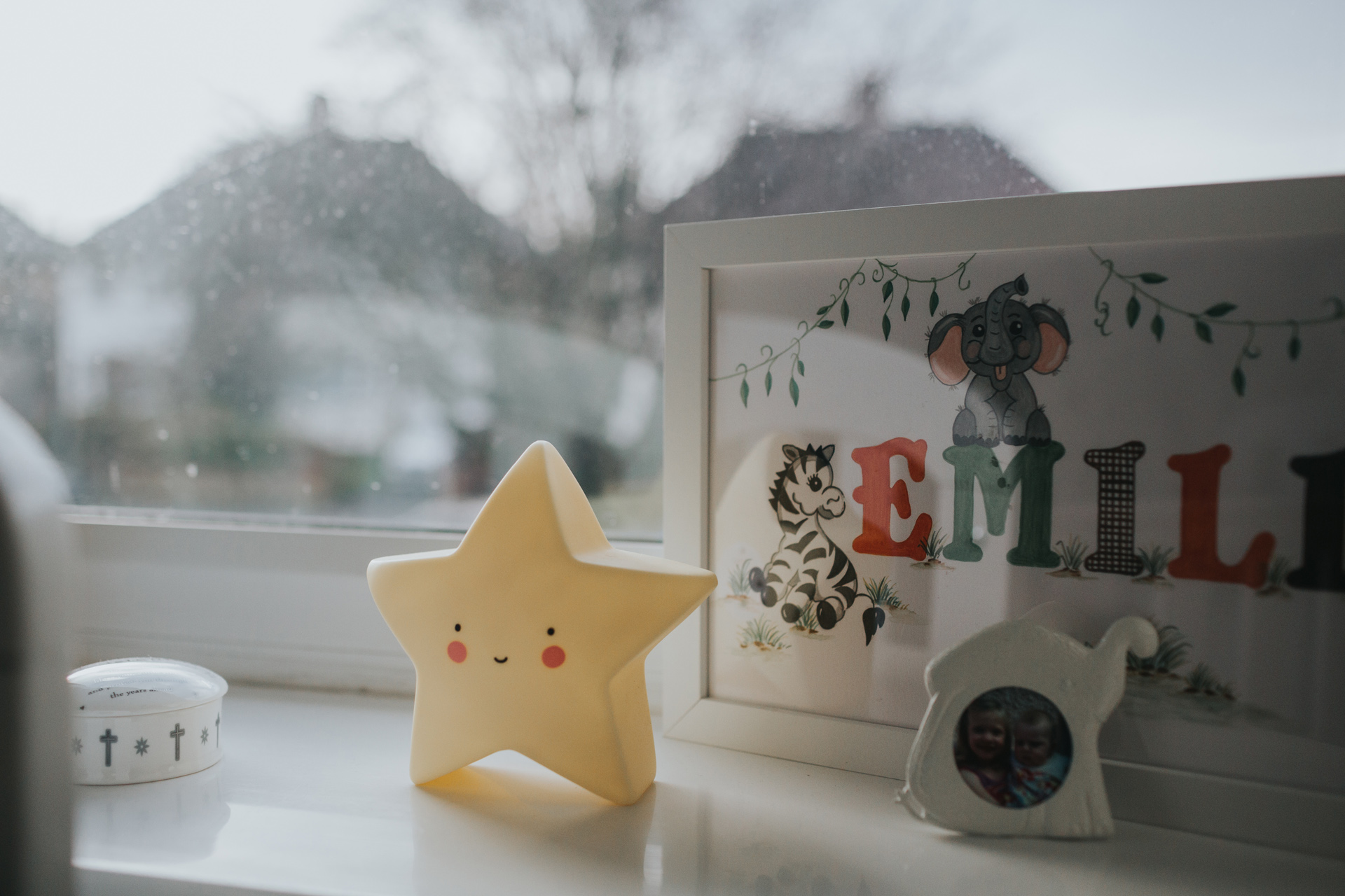 A smiling star toy stands on a windowsill of a child's room, the view of the liverpool street outside can be seen. 