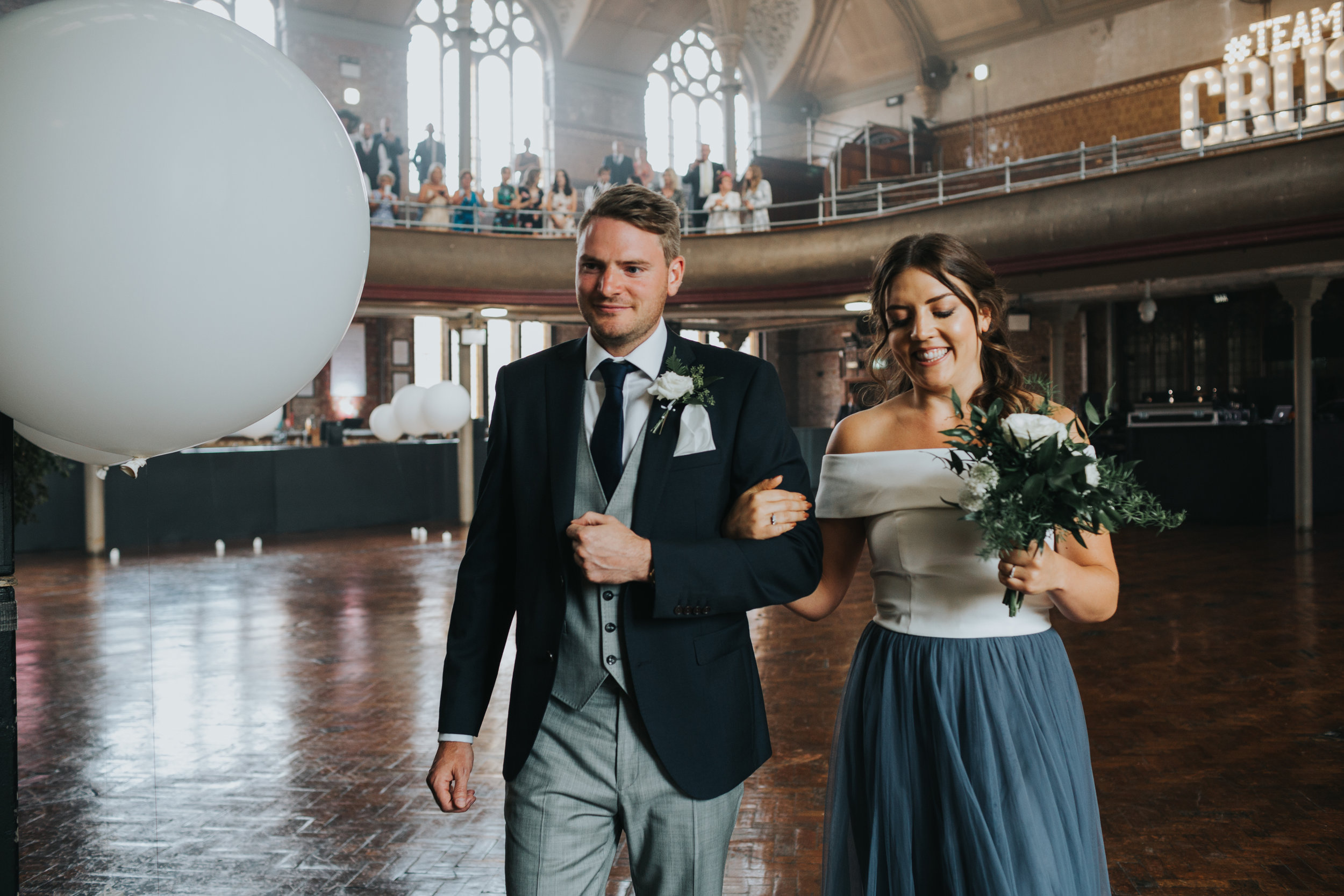 Bridesmaid and groomsmen walk together across the hall. 