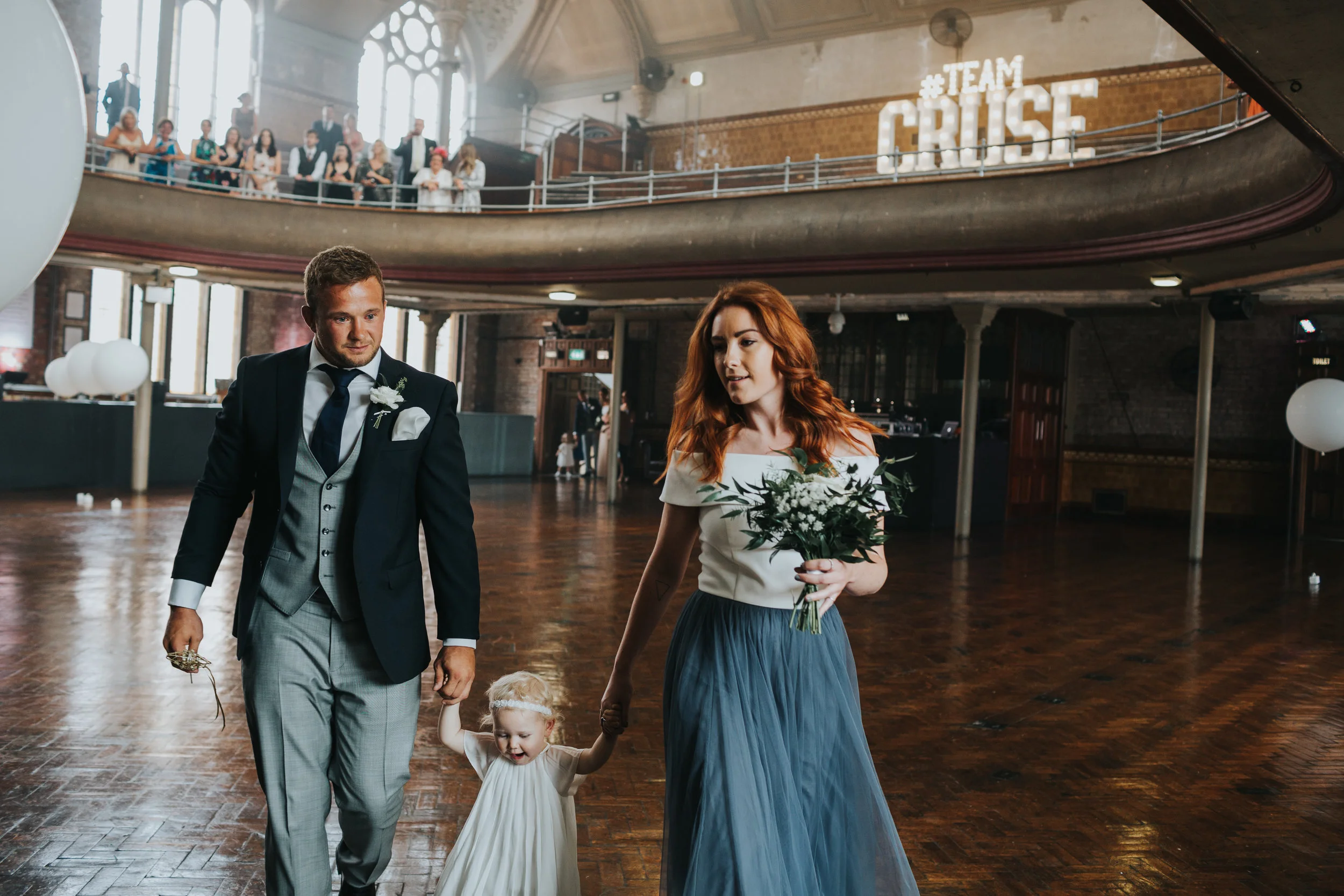 Bridesmaid and groomsmen walk flower girl Matilda to the stage in the Albert Hall, Manchester.