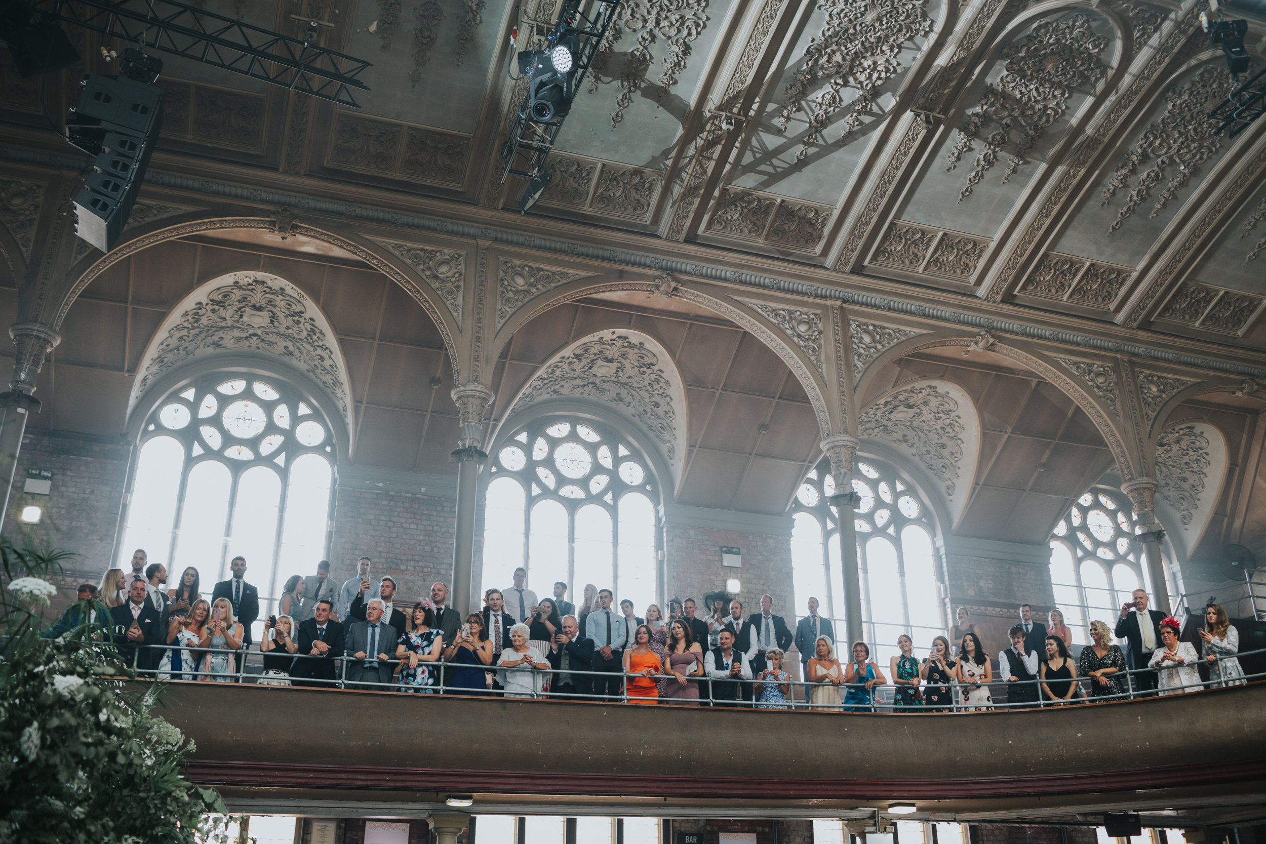 Wedding guests stand cheering from stalls. 