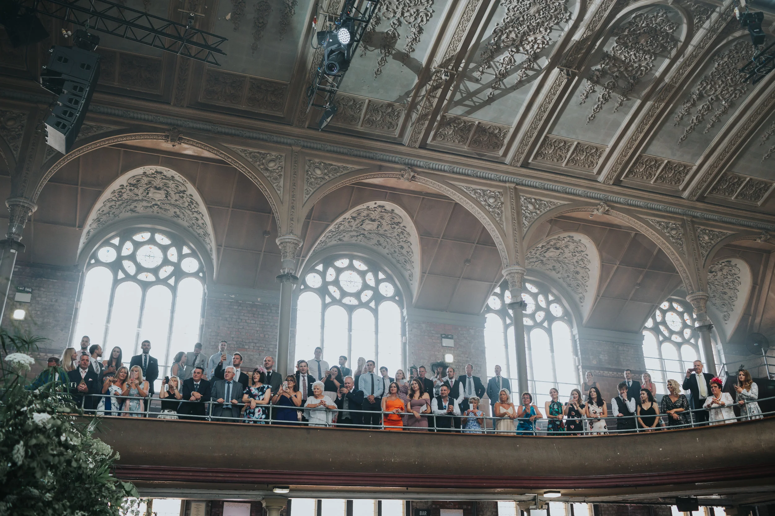 Wedding guests stand cheering from stalls.