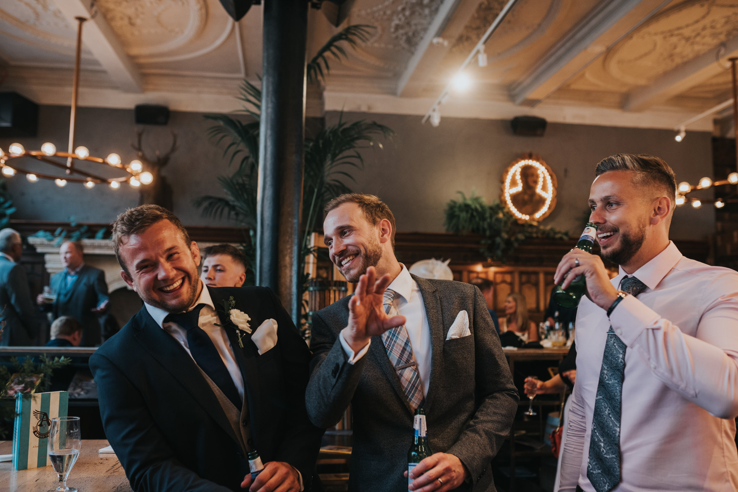 Three male wedding guests laugh together. 