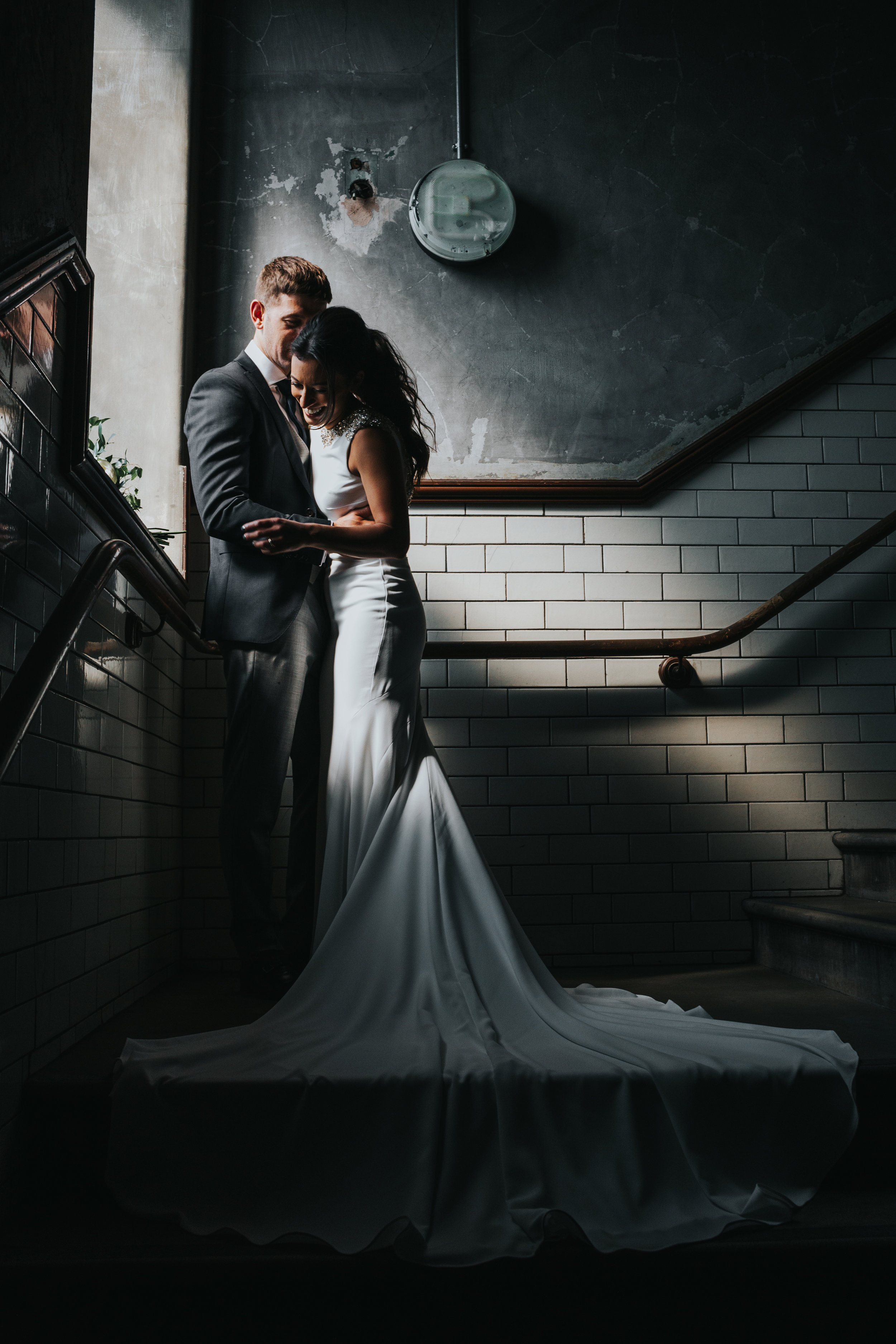 Bride and groom laugh in pocket of window light, Albert Hall Manchester.