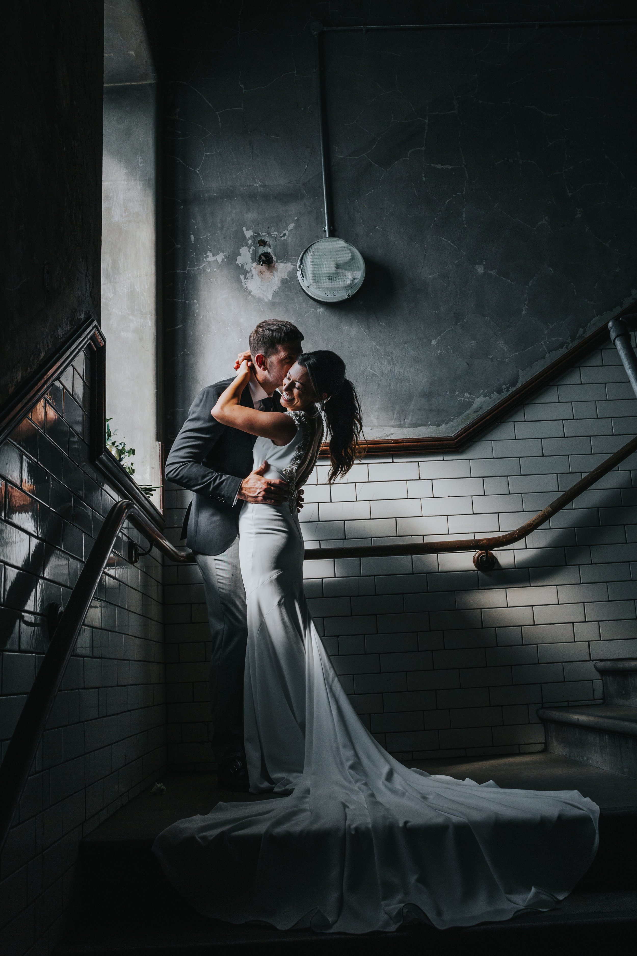 Couple embrace in a pocket of strong window light. 