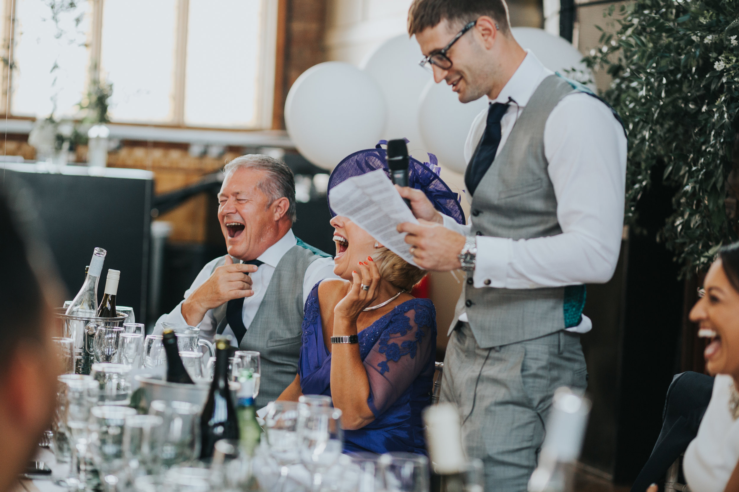 Groom makes his speech as his parents laugh. 