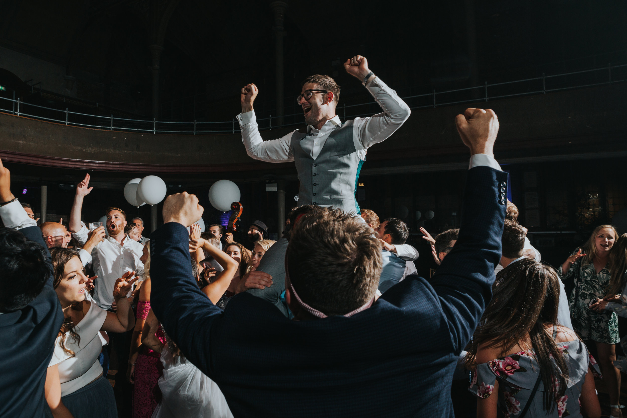 Groom sits on his friend shoulders with his hands in the air at The Albert Hall, Manchester.