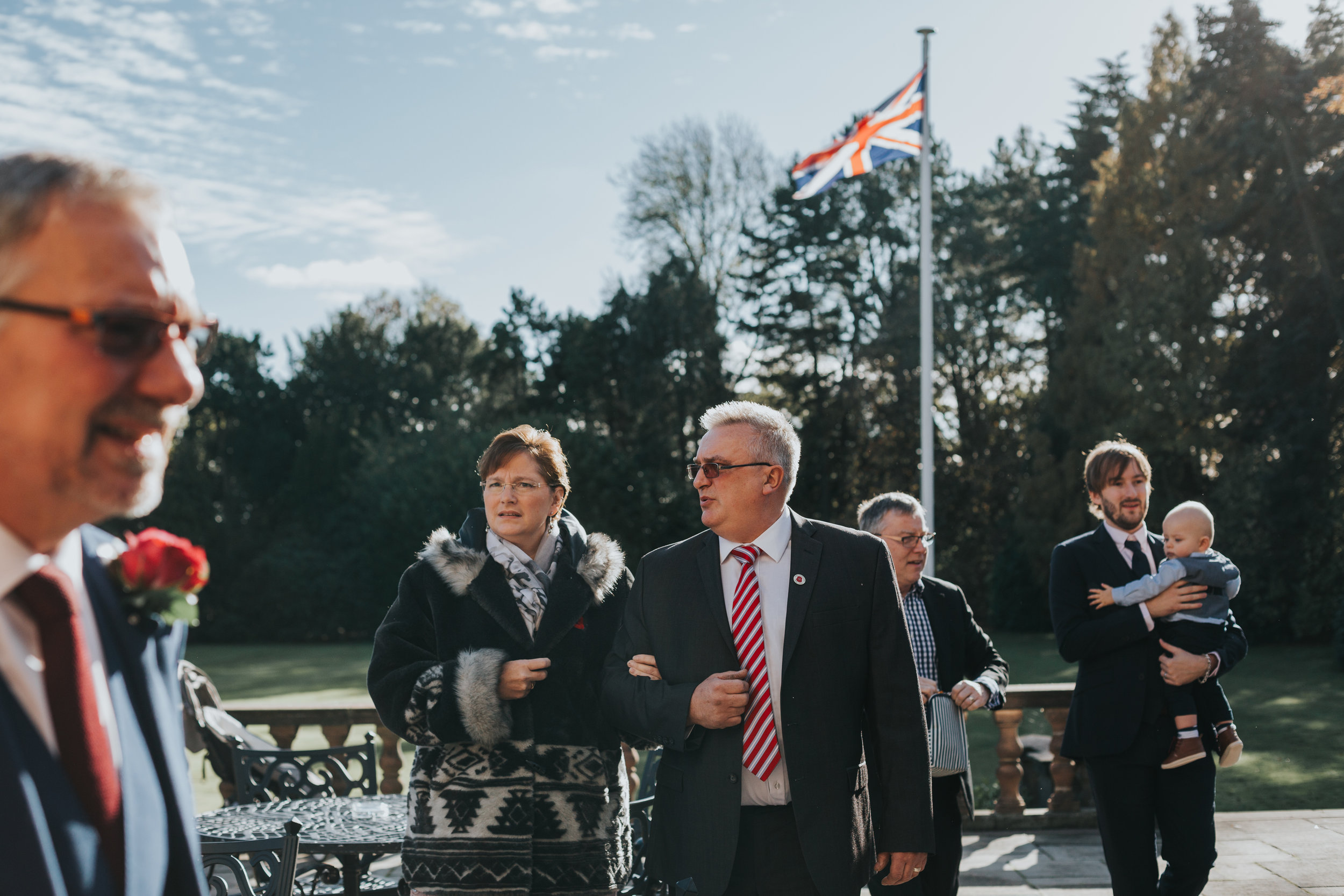 Guests take their seats at the outdoor wedding ceremony, the Union Jack Flag flies behind them.