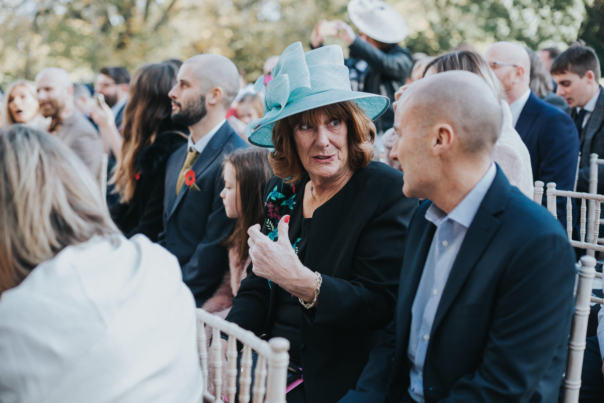 Wedding guests in blue hat chats with her friend. 