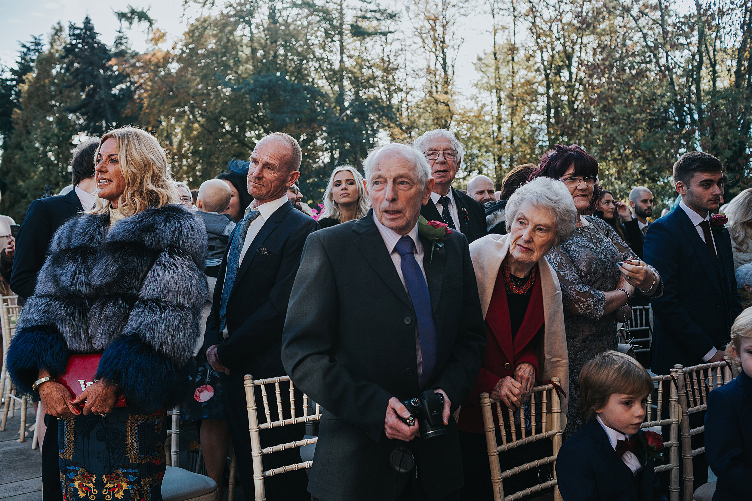 The guests stand up and watch as the bride makes her way towards them at an outdoor wedding ceremony at Inglewood Manor. 