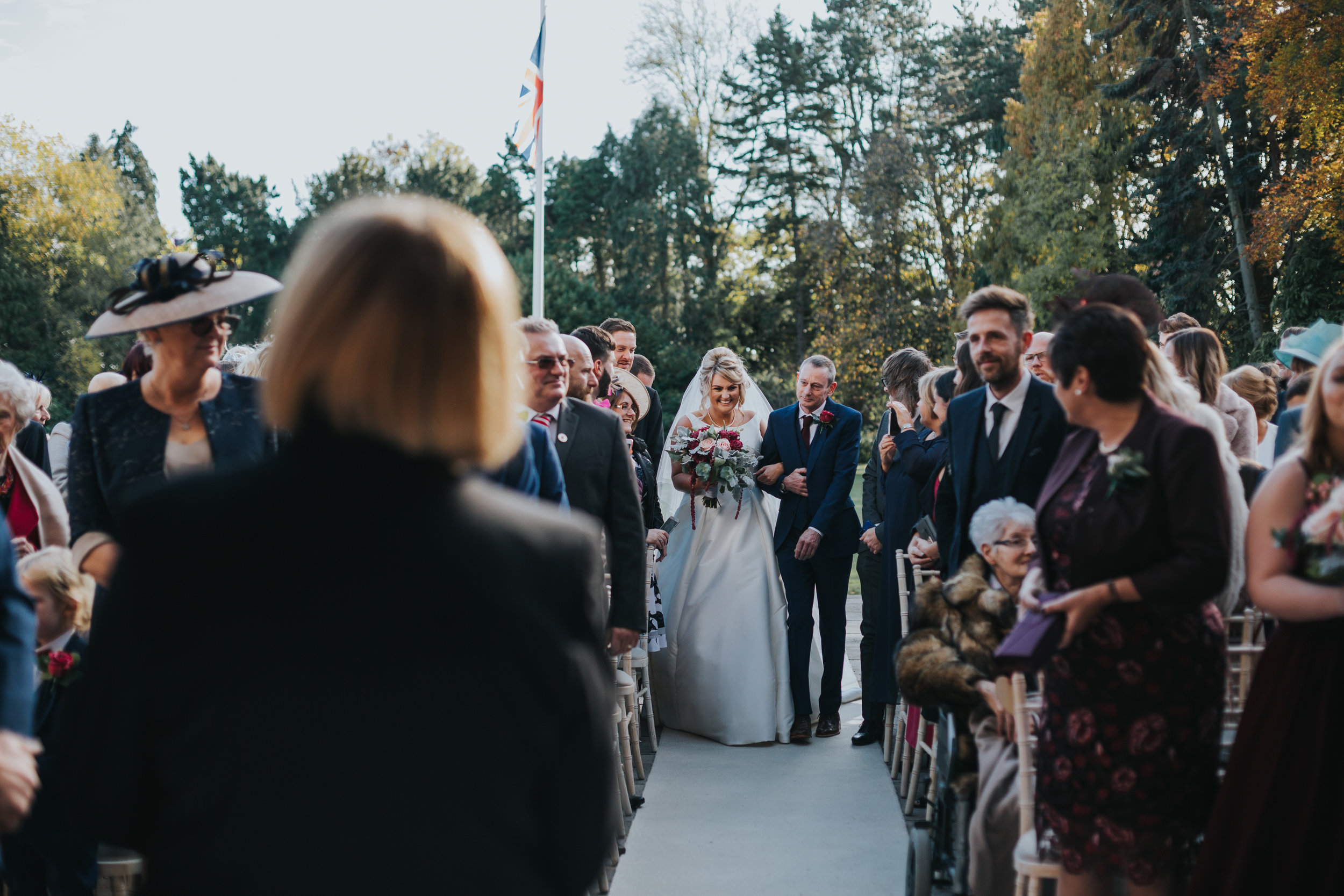 The Bride makes her way down the aisle, arm in arm with her father during an outdoor ceremony at Inglewood manor. 