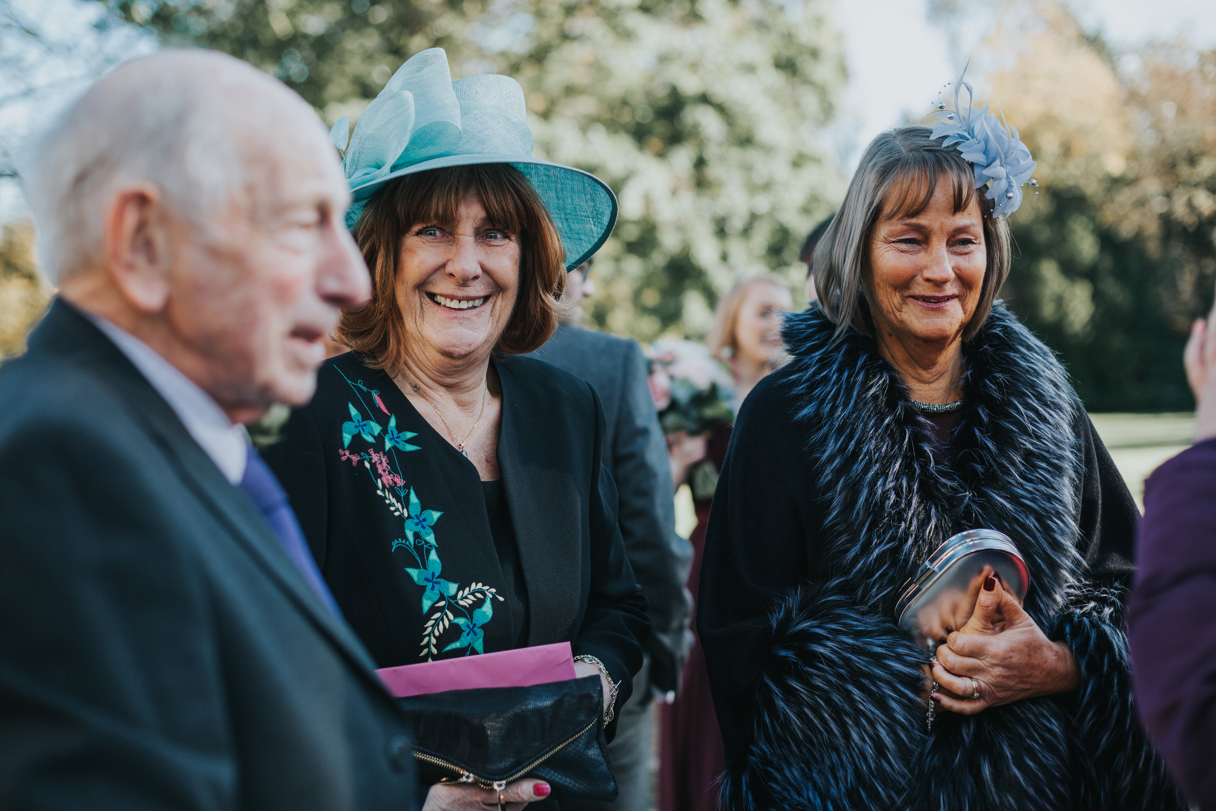 Guests smiling in the sun shine wearing fancy hats.
