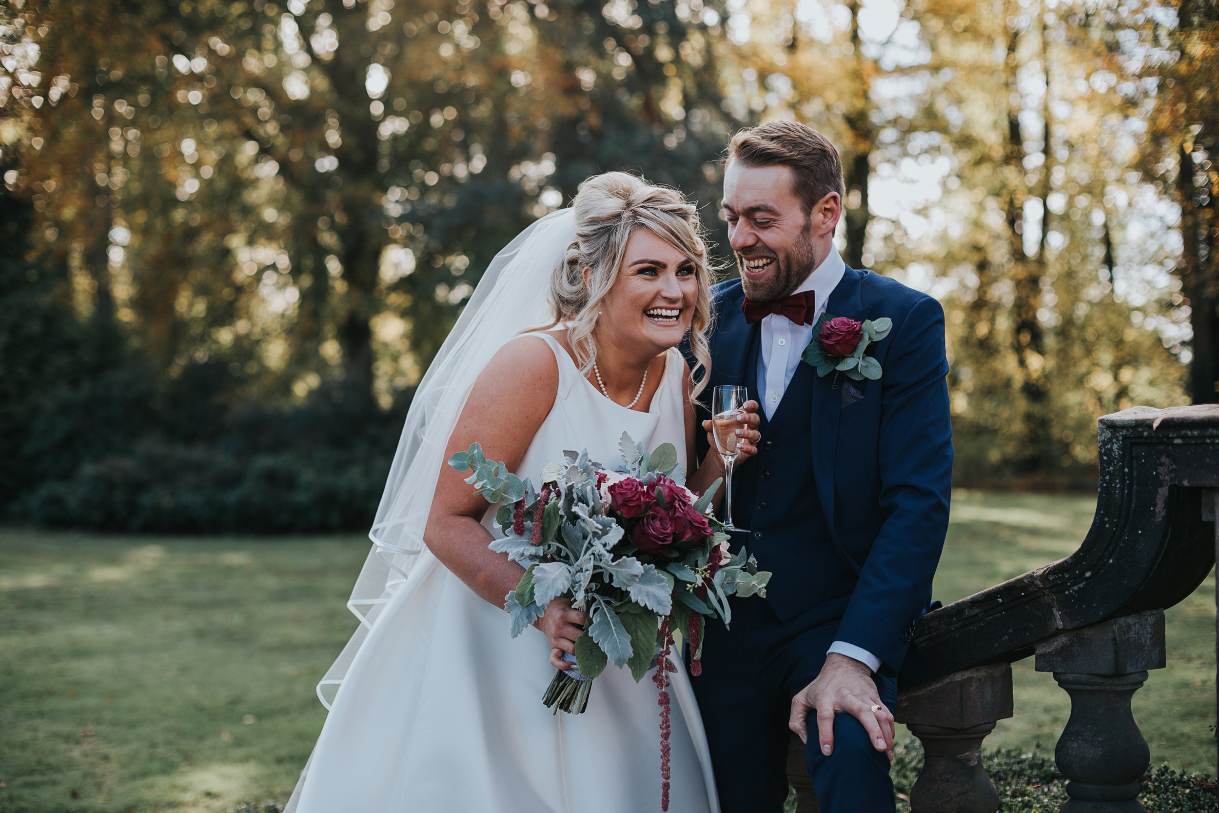 Bride and Groom laugh together on the steps on Inglewood Manor, the yellow light of the trees behind them.