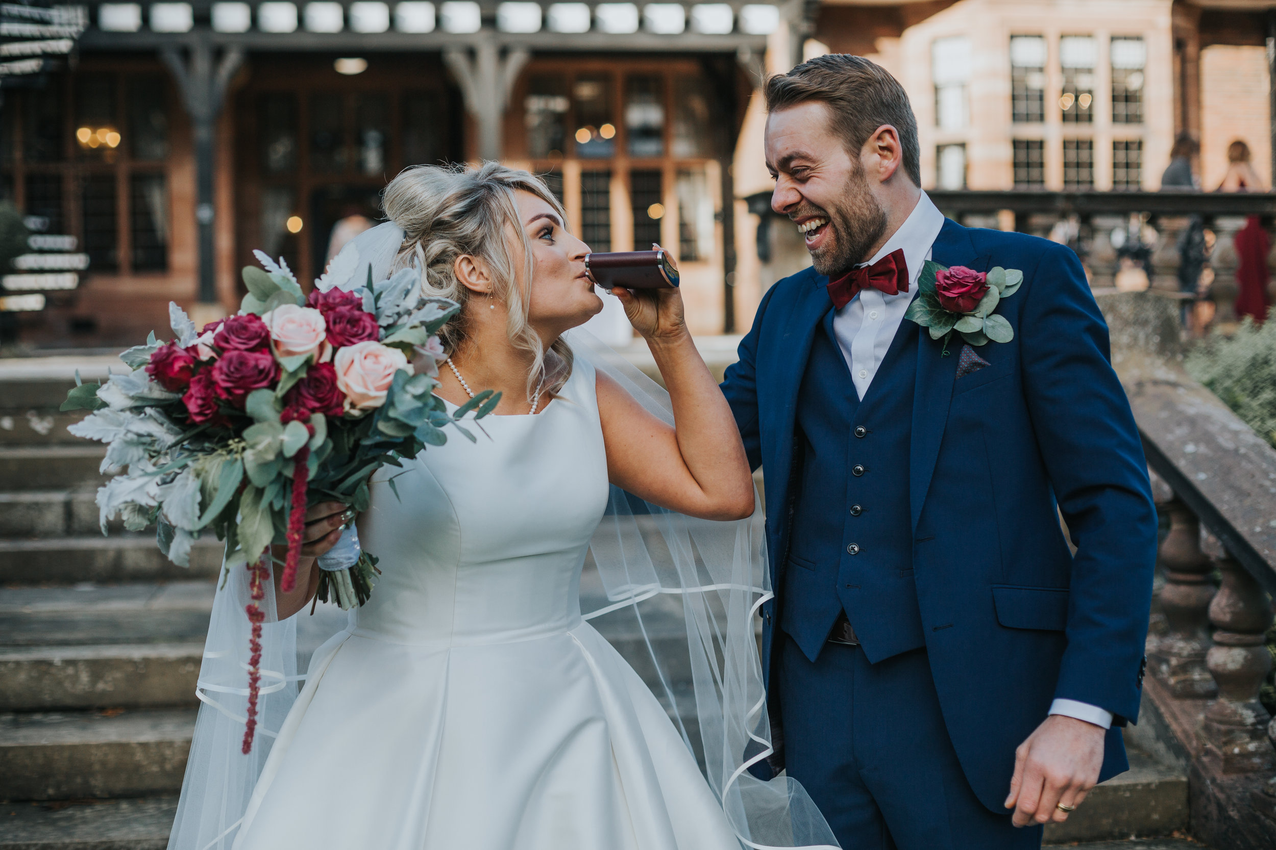 Bride takes a sqwig from her husbands hip flask as he laughs on the back steps of Inglewood Manor. 