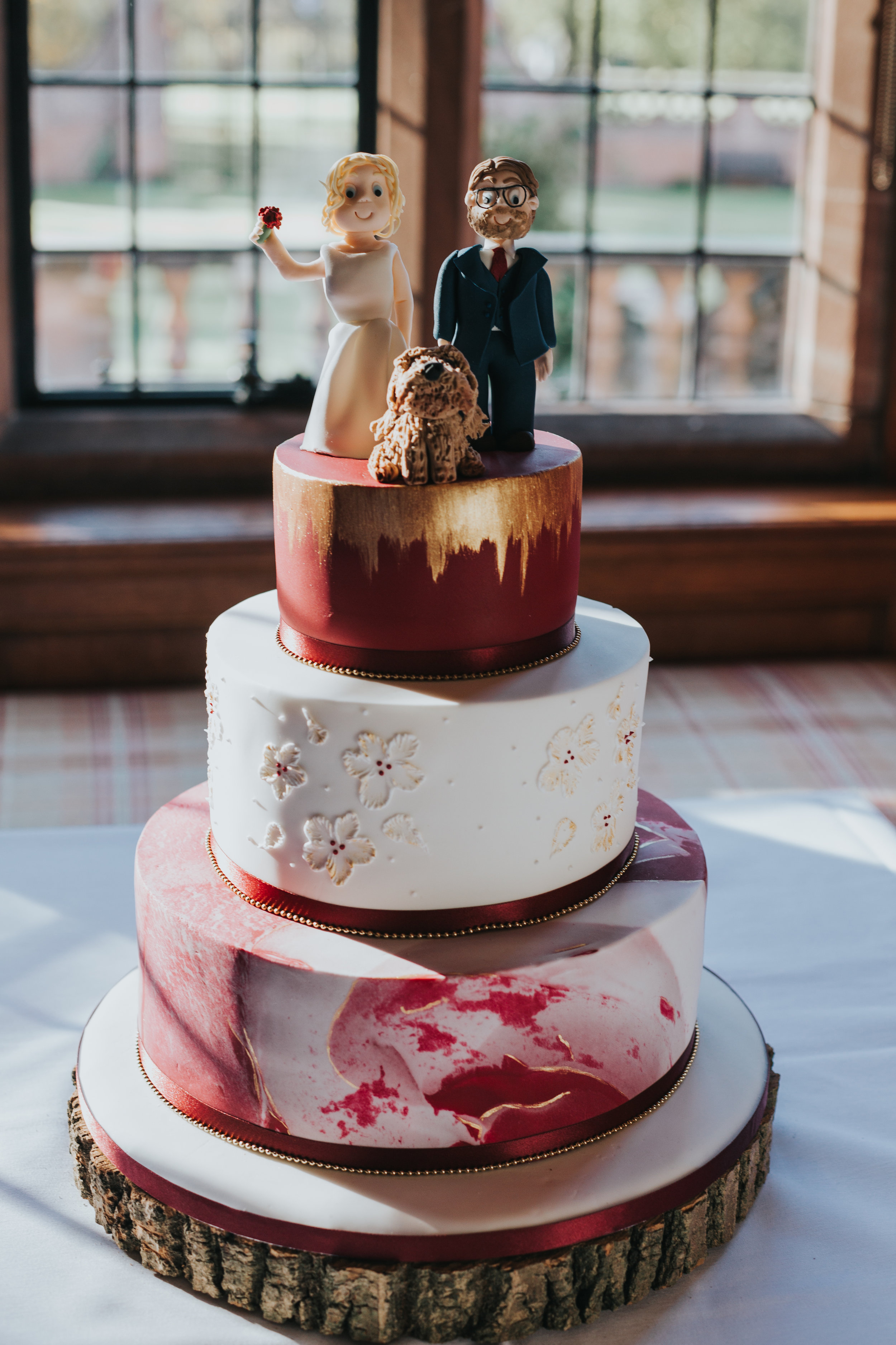 Red and white wedding cake topped with the bride and groom and their dog. 