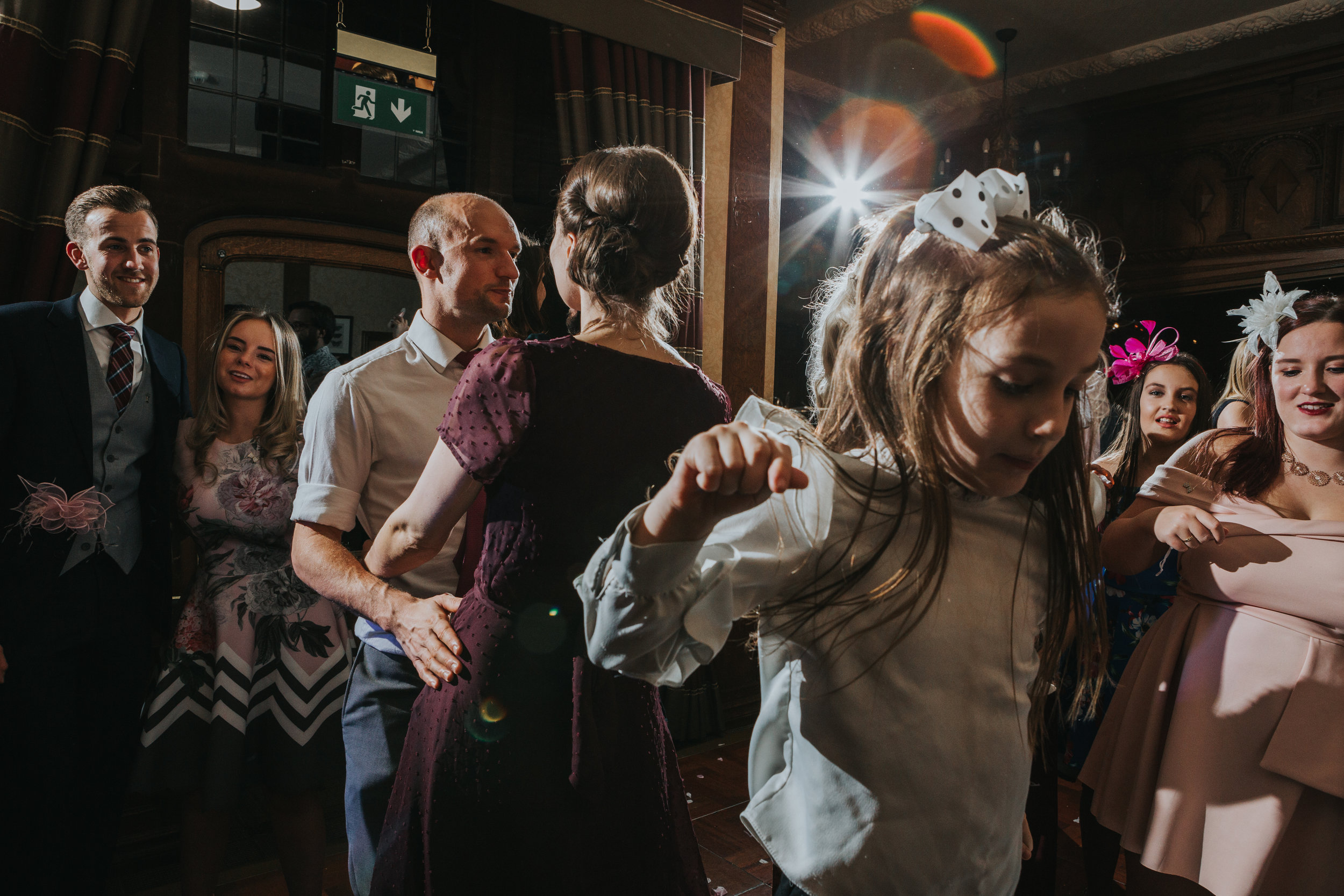 Wedding guests hit the dance floor, a little girl jumps up and down as wedding guests dance behind her. 