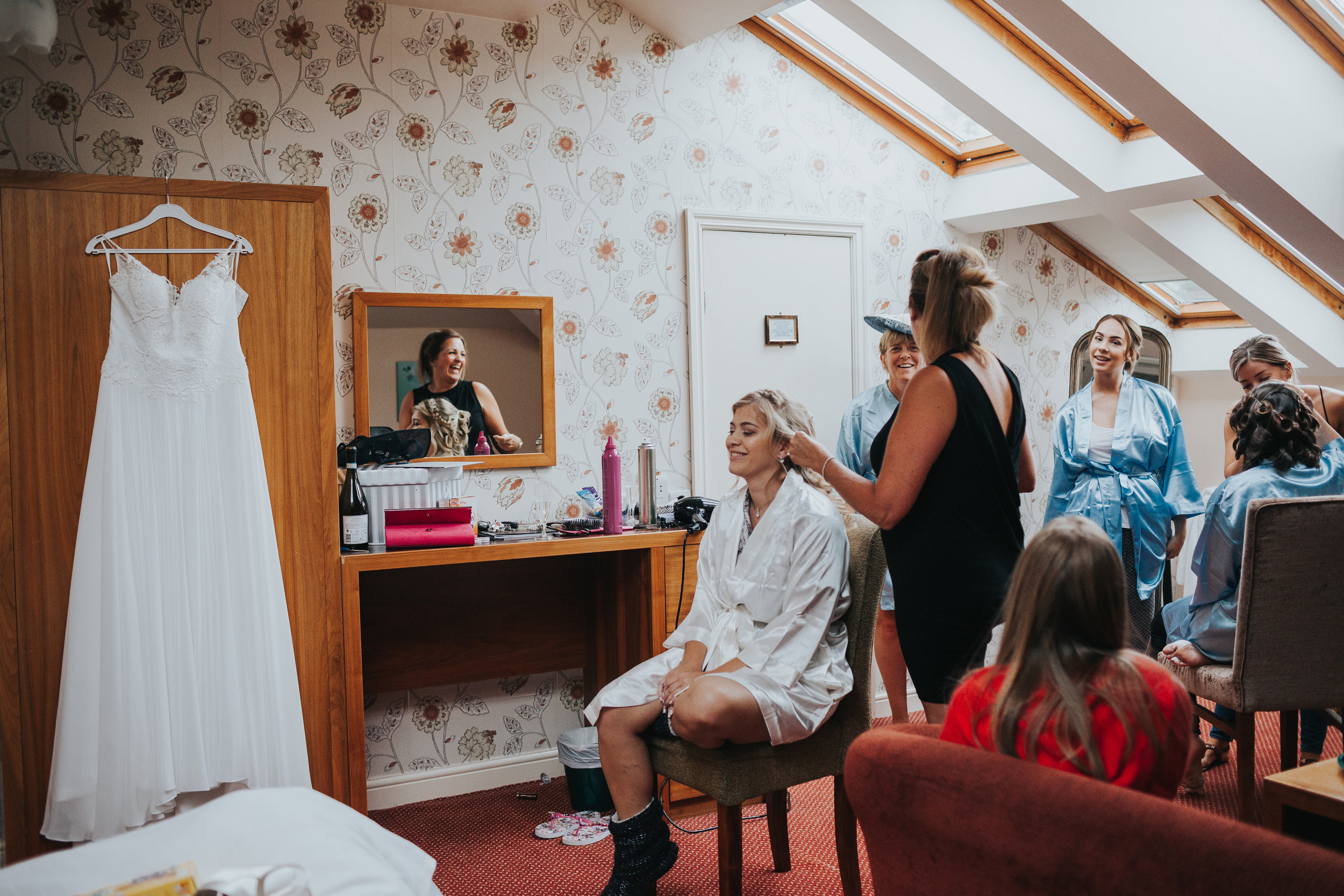 Bride gets her hair done while looking at her wedding dress. 