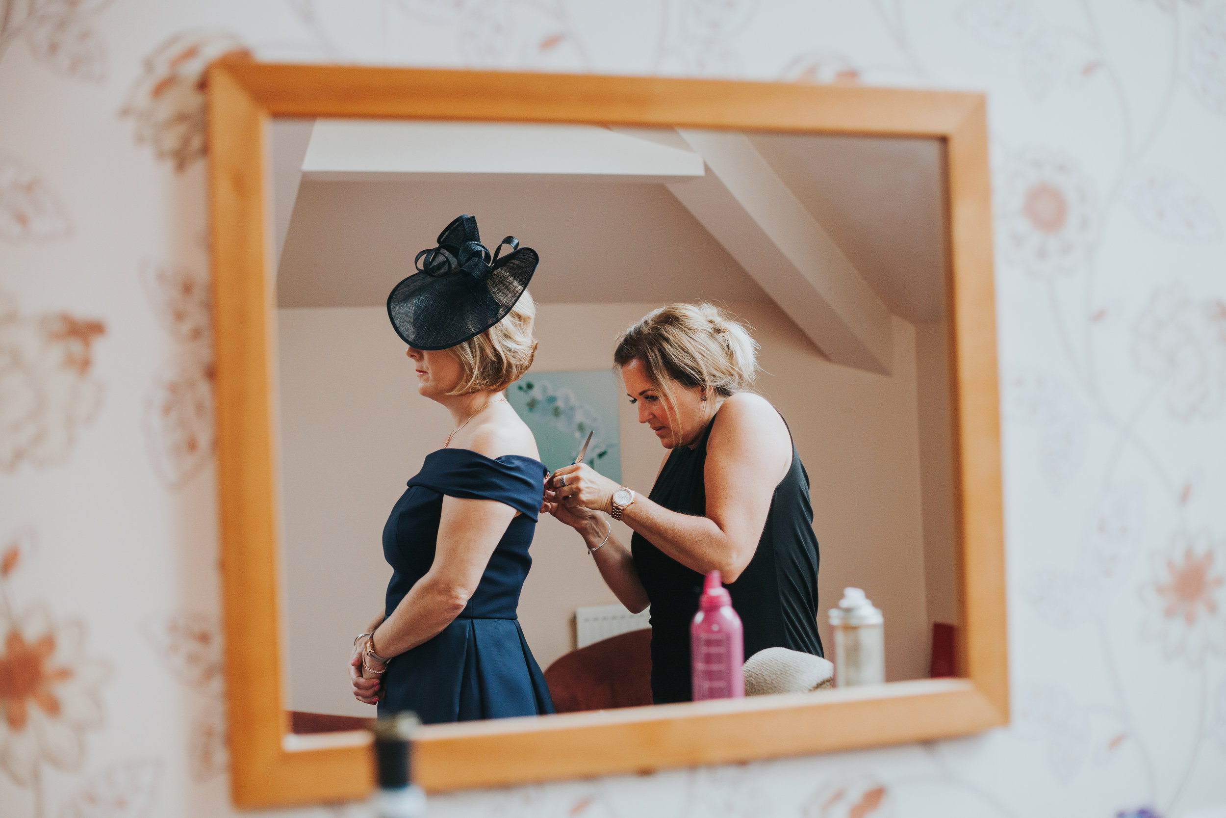 Female wedding guest is helped into her dress.