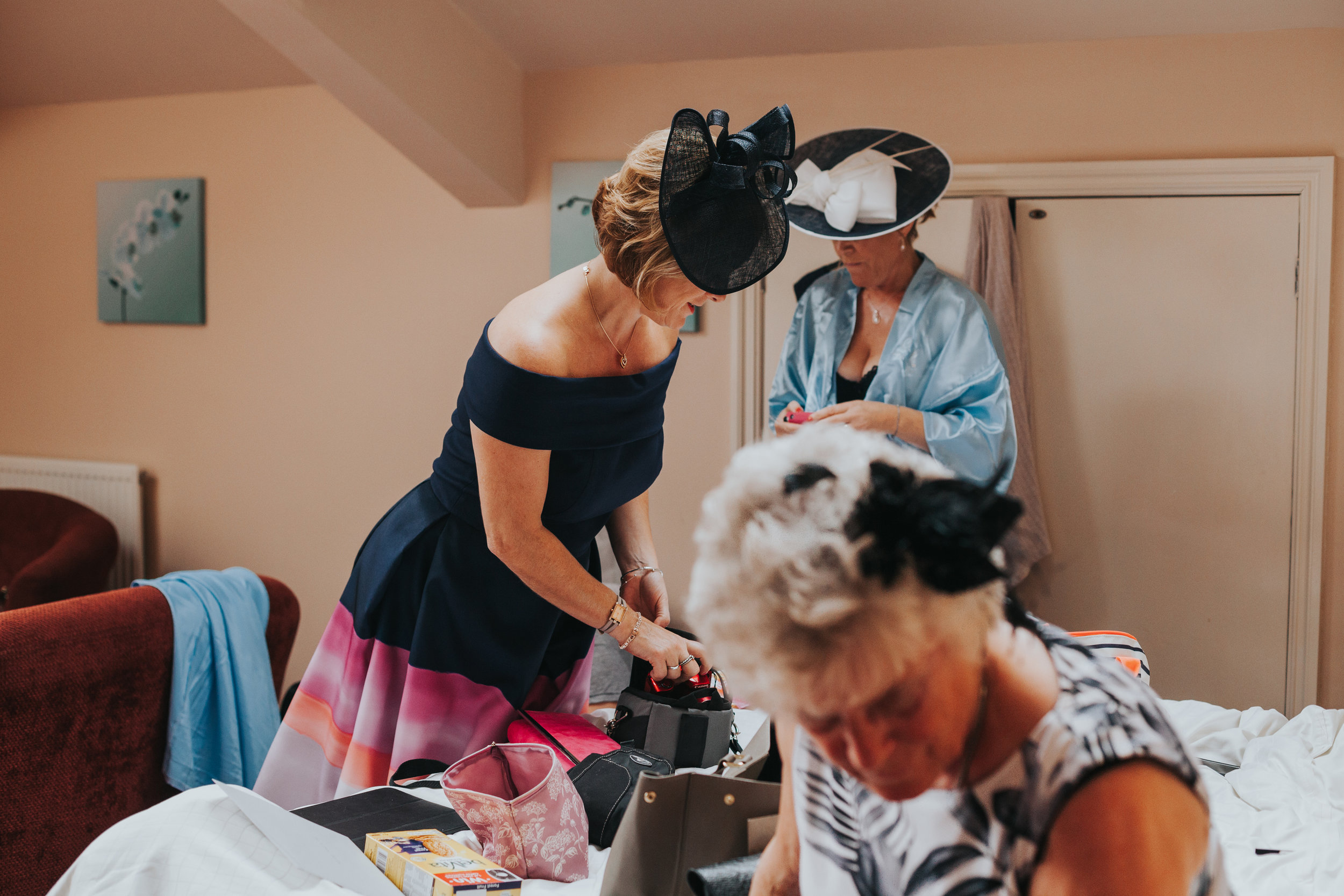 Ladies beding over to get ready all wearing wedding hats and  making a triangle. 