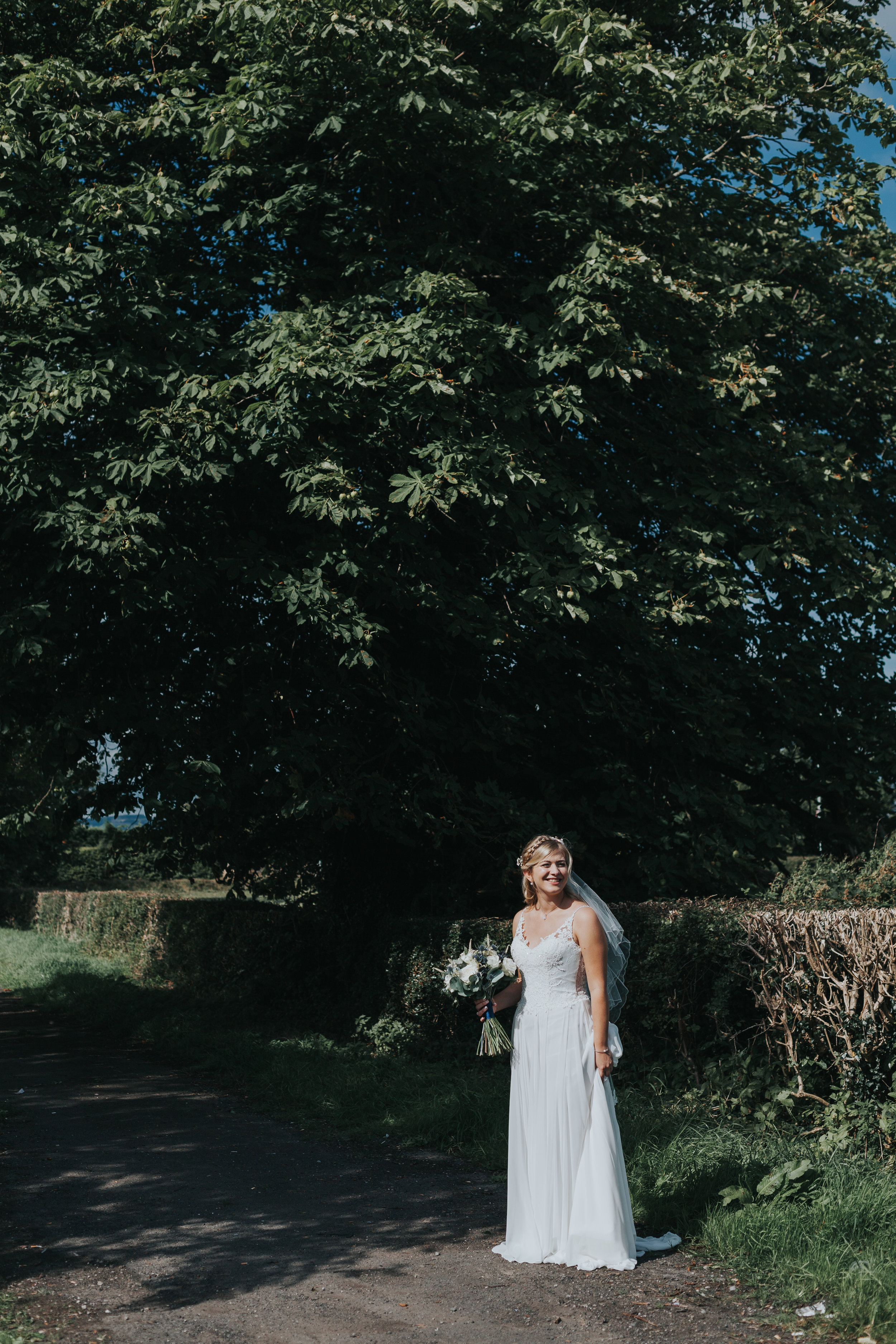 Bride stands alone under a big tree.