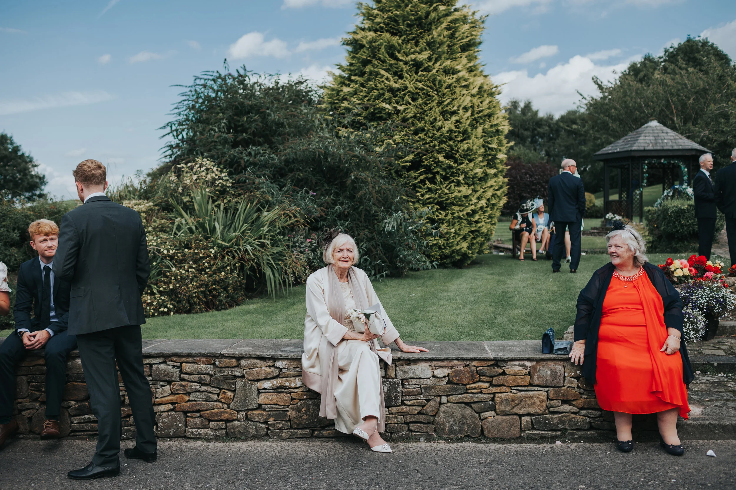 Wedding guest sits on a wall staring straight at the camera. 