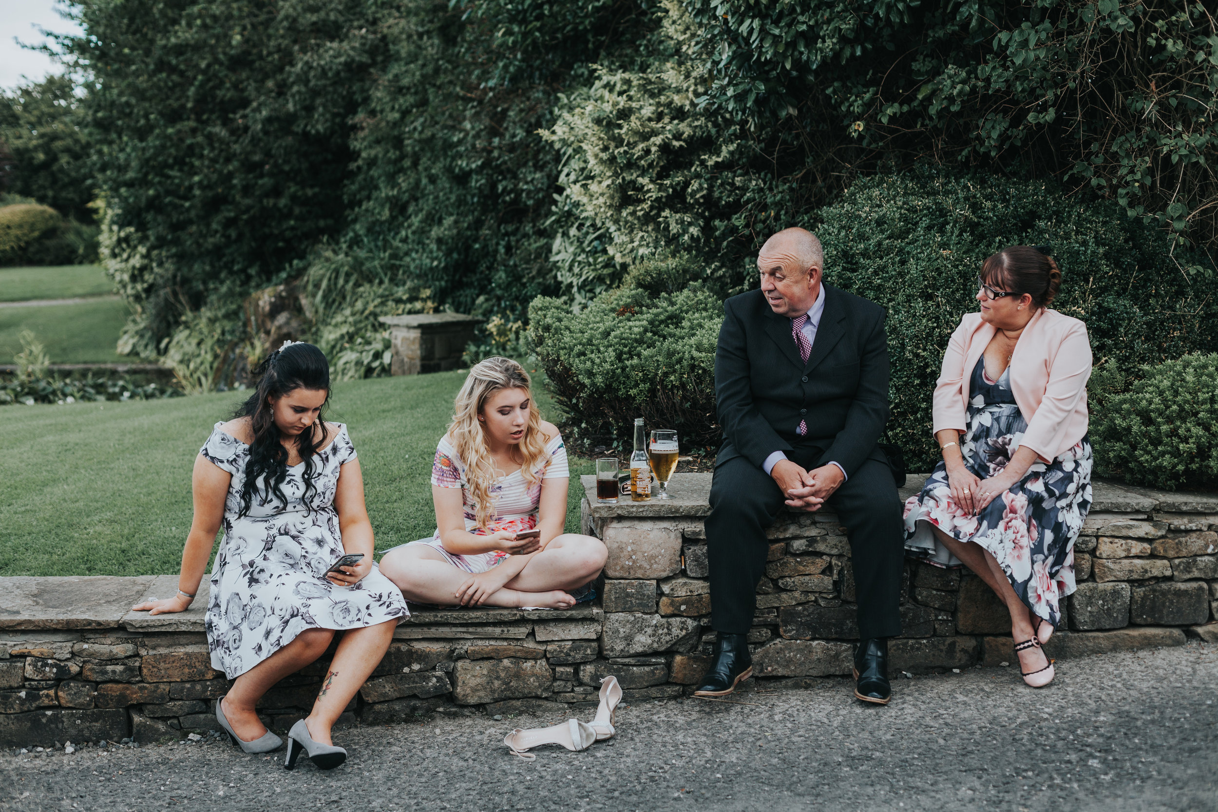 Four wedding guests sit together, one has given up on her shoes already. 