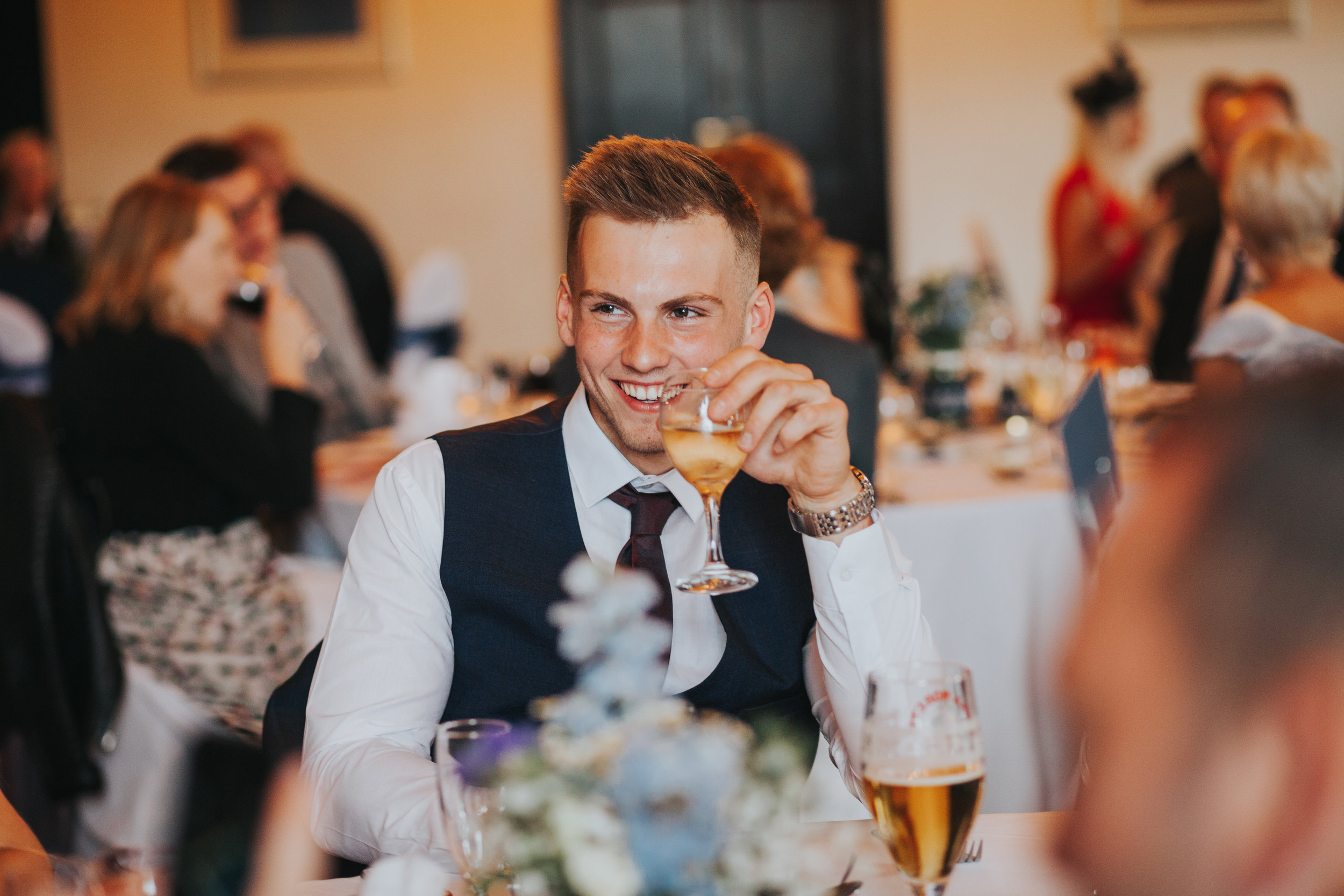 Male wedding guest enjoys some champagne while smiling. 