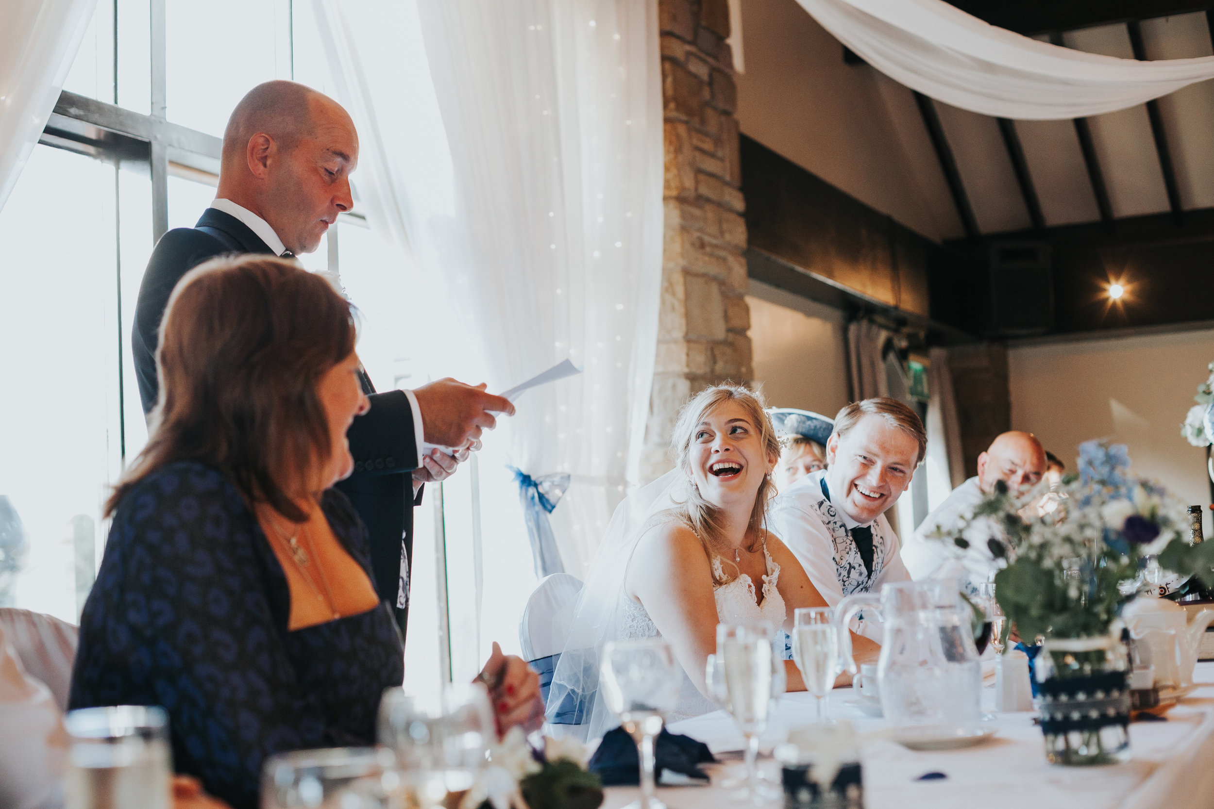 Bride laughs as her father gives a speech. 