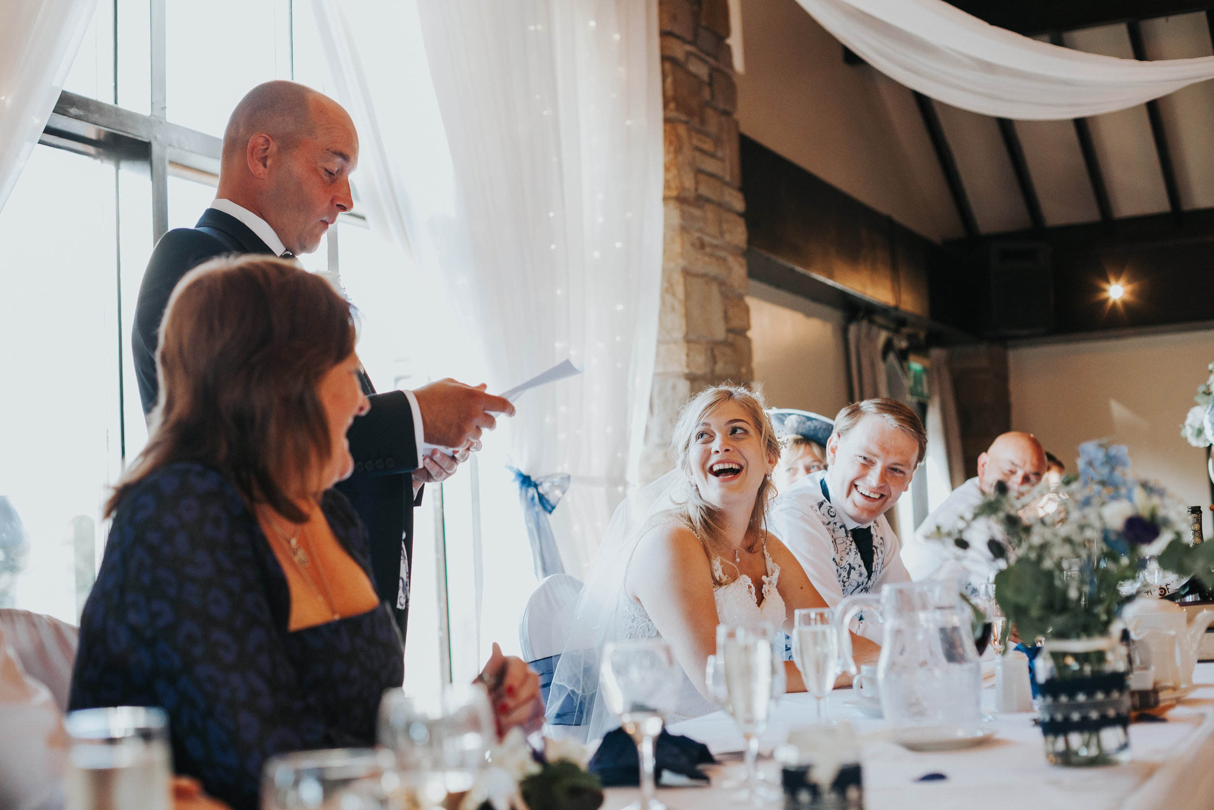 Bride laughs as her father gives a speech.