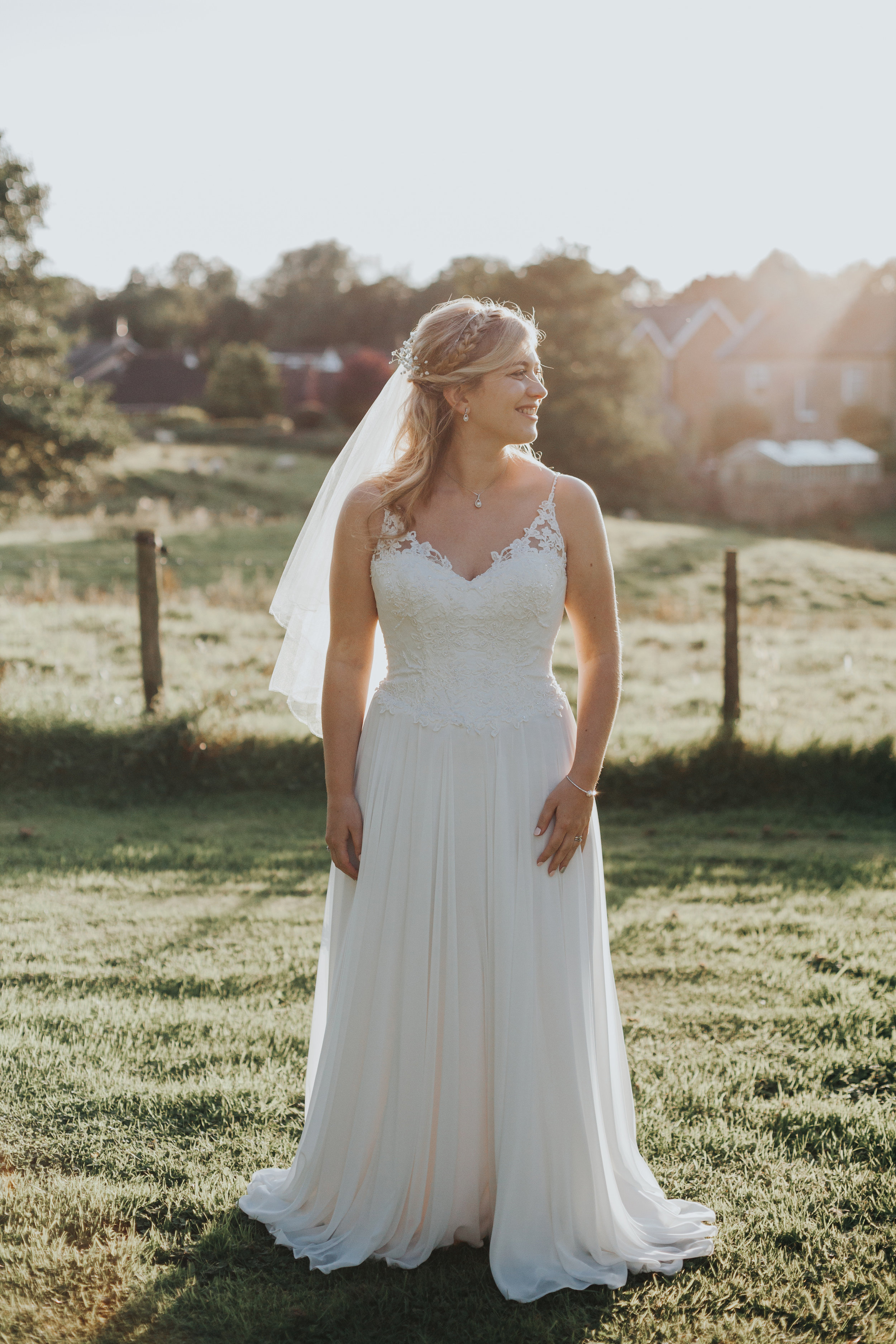 Bride stands in hazy sunlight smiling.