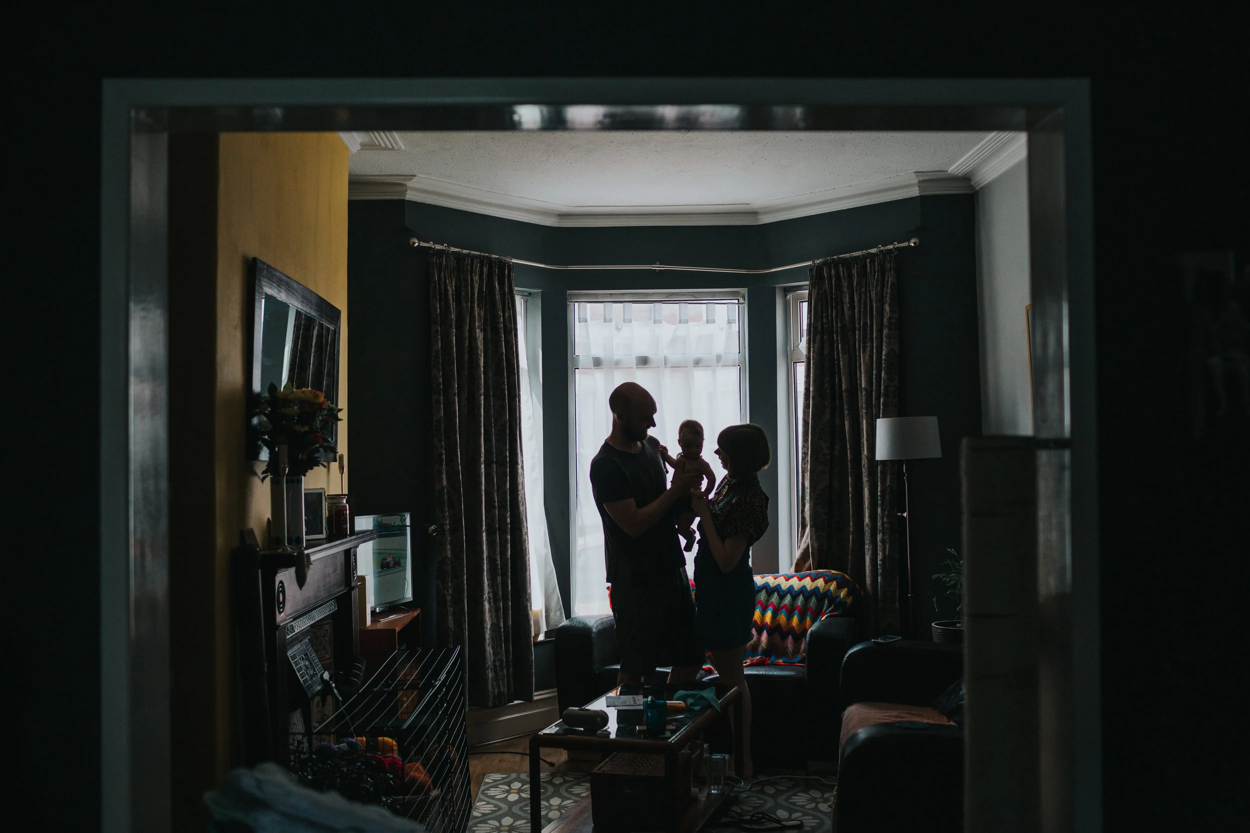 Family stand together in front of a bay window in their family home in Liverpool. 
