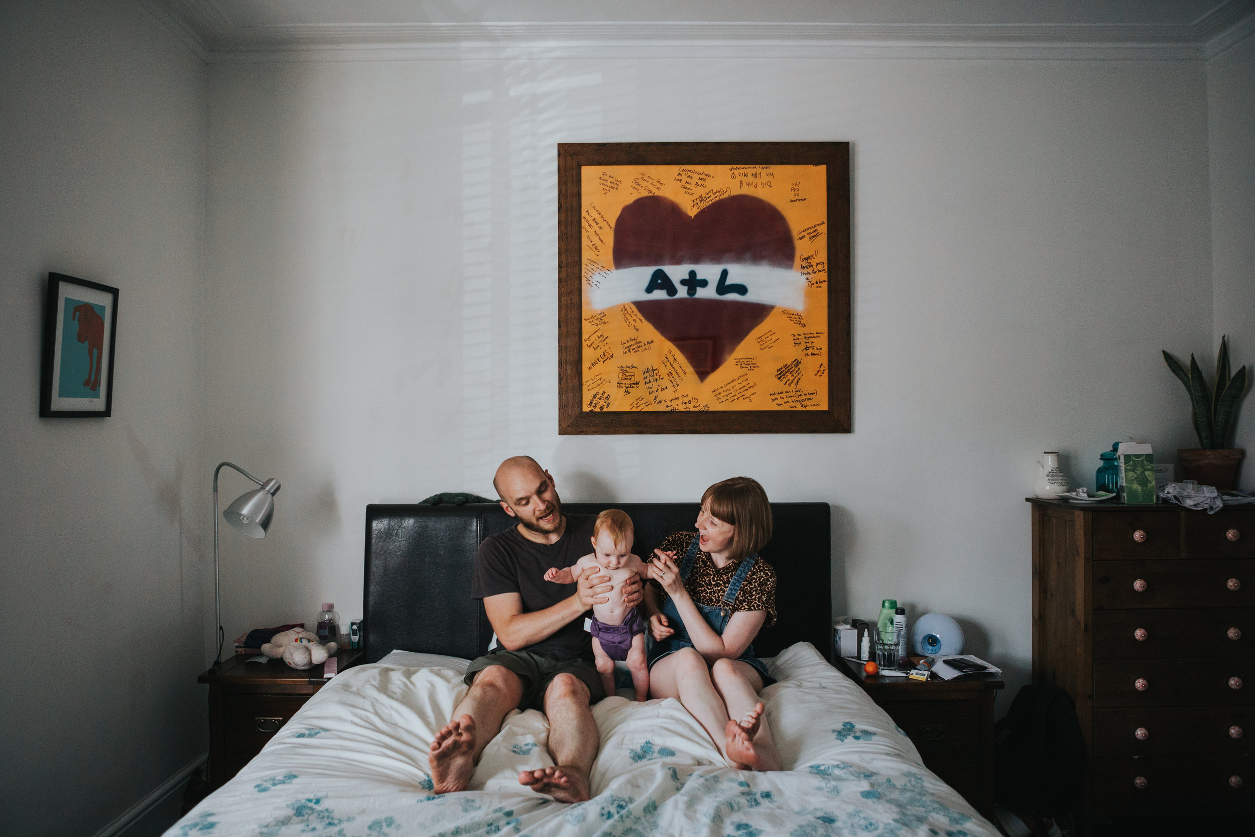 Family sit on Mum and Dad's bed under graffiti art canvas at their home in Liverpool. 