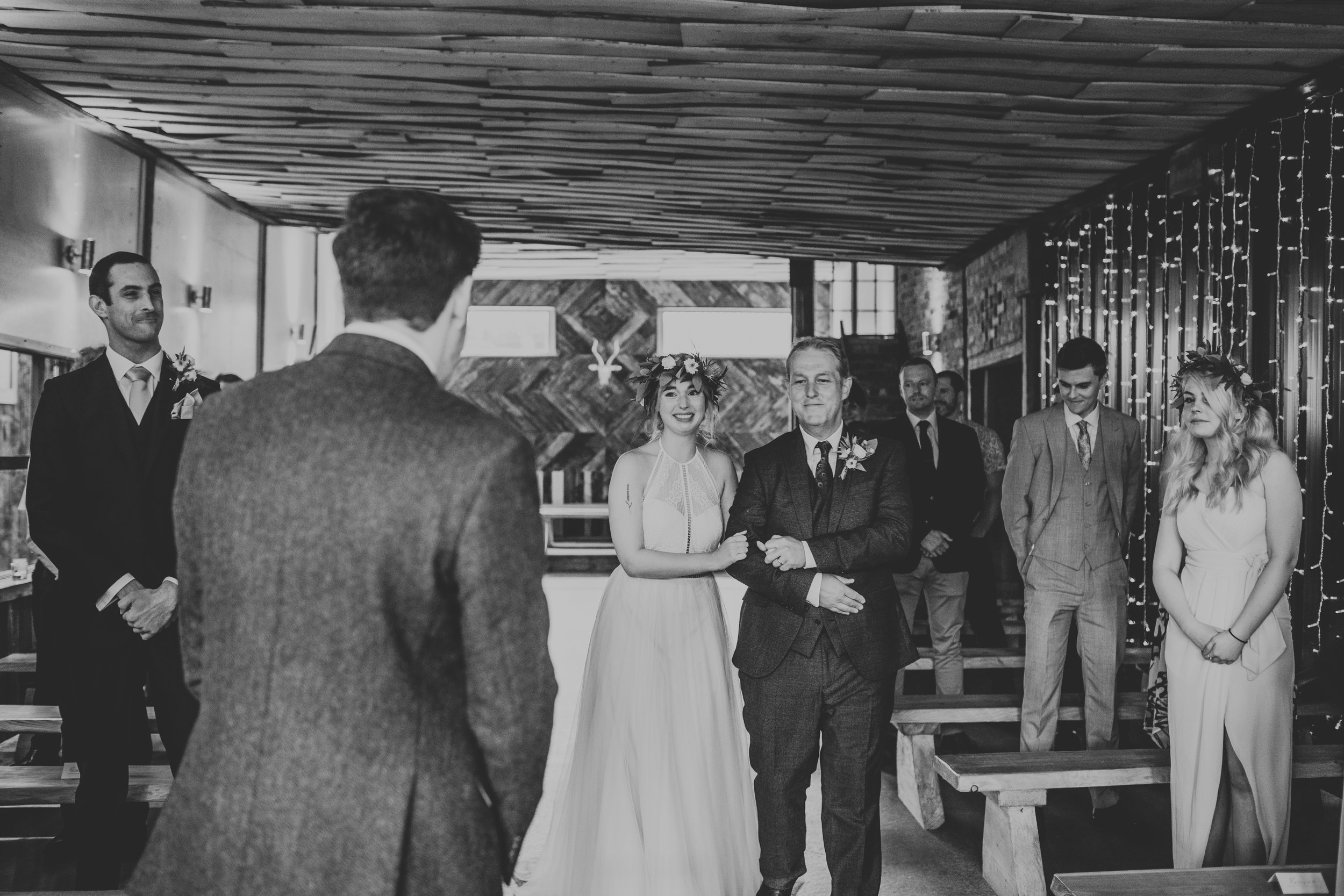 Bride is walked down the aisle by father. Photograph in black and white. 