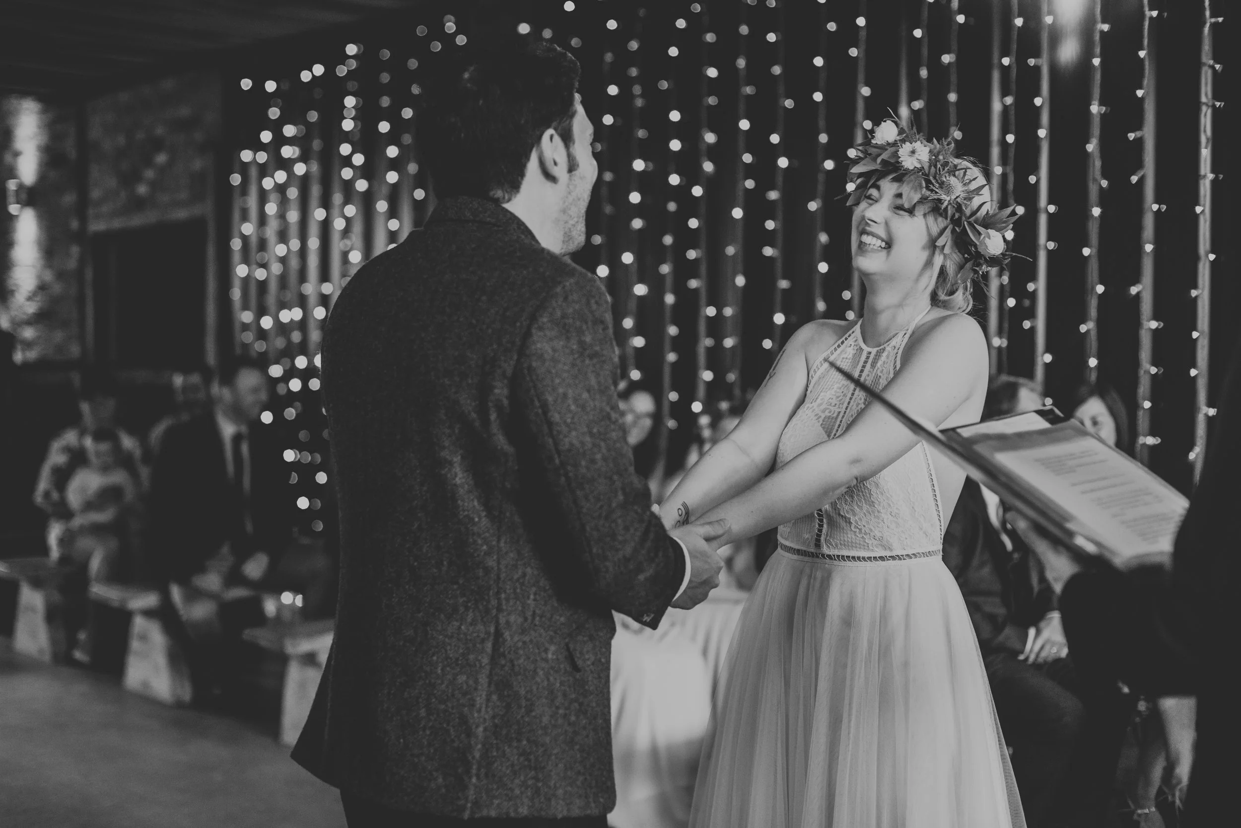 Bride and groom hold hands and laugh together, photo in black and white. 