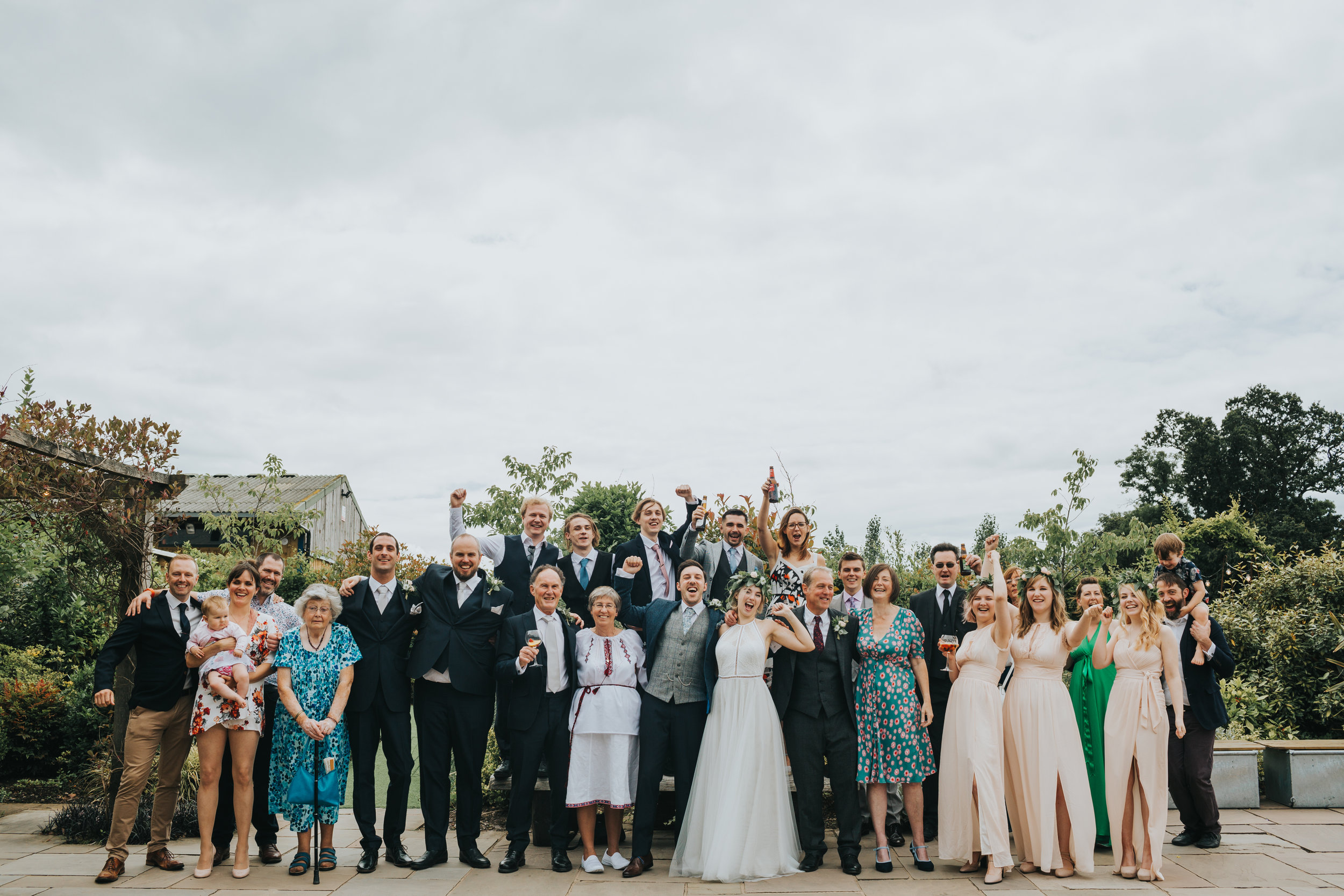 Group photograph of all the wedding guests cheering at Owen House Wedding Barn. 