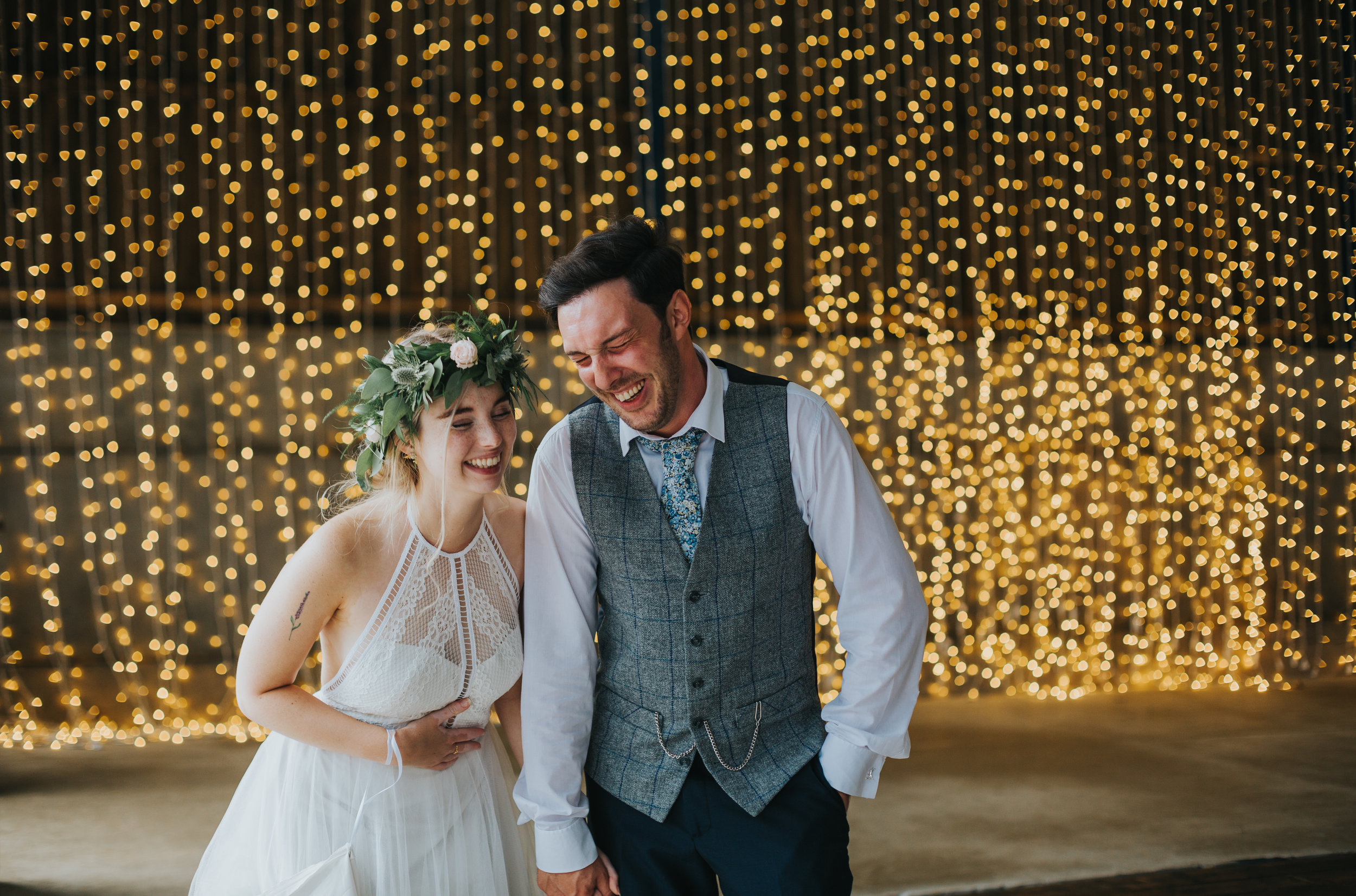 Bride and groom laugh in font of fairy lights in Owen House Wedding Barns Shooting Barn. 