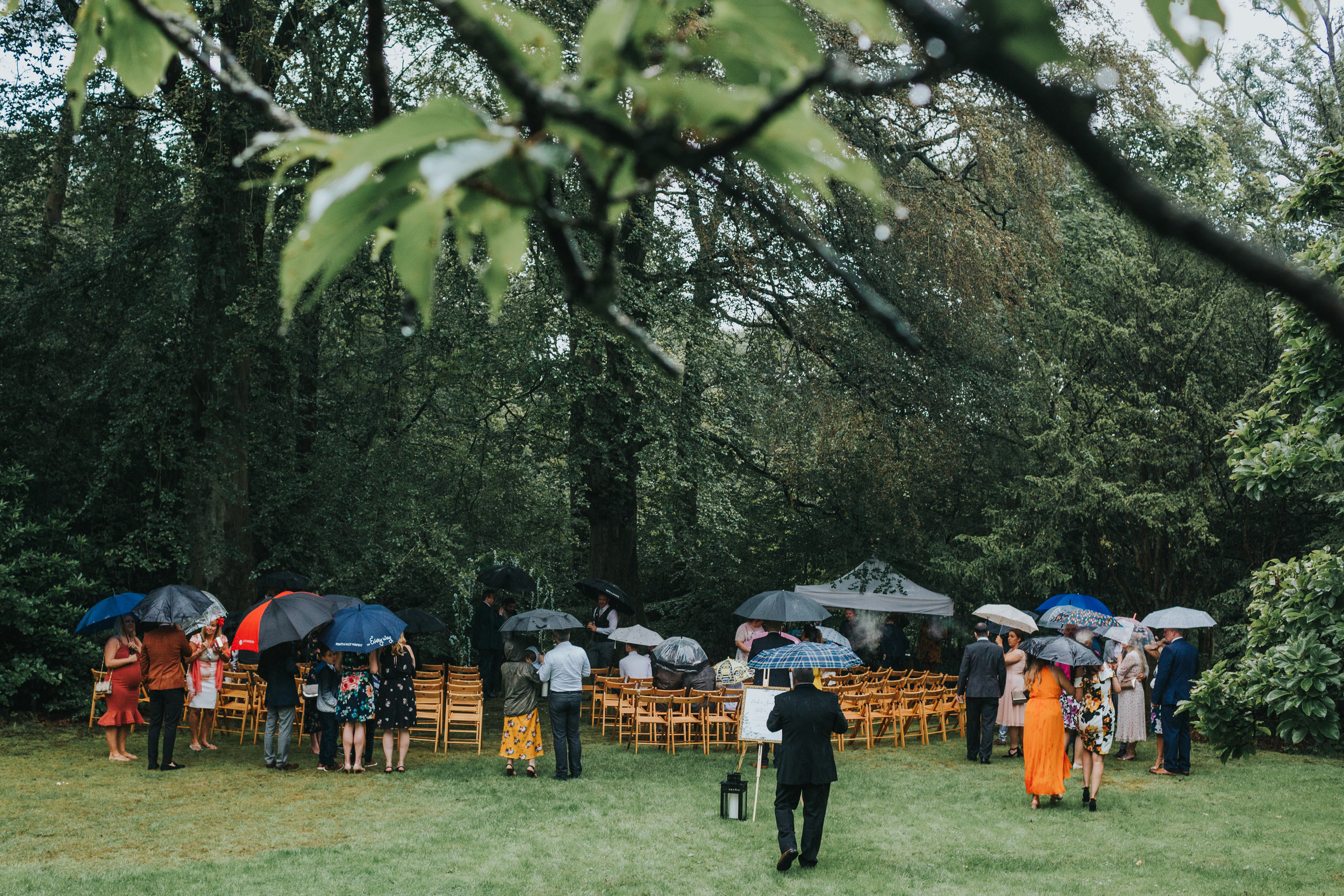 Wedding guests gather with their brollies for an outdoor ceremony at Spring Cottage