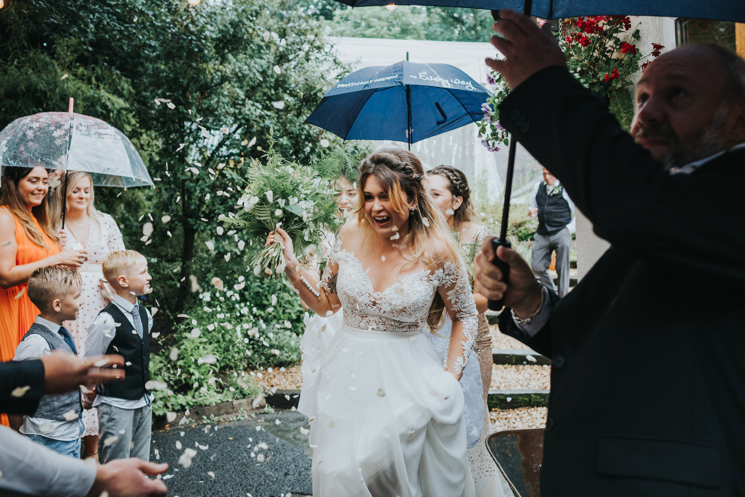 Bride makes her way out under a sea of brollies held for her by wedding guests as they throw confetti.