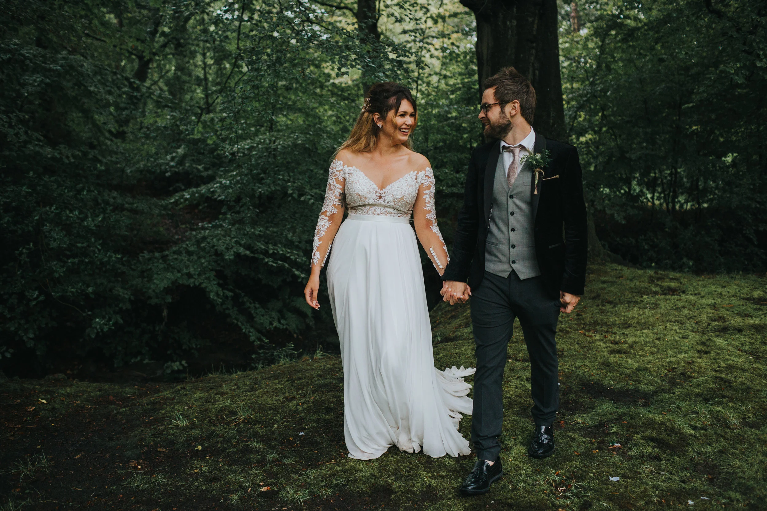 Bride and groom walk together under the trees. 