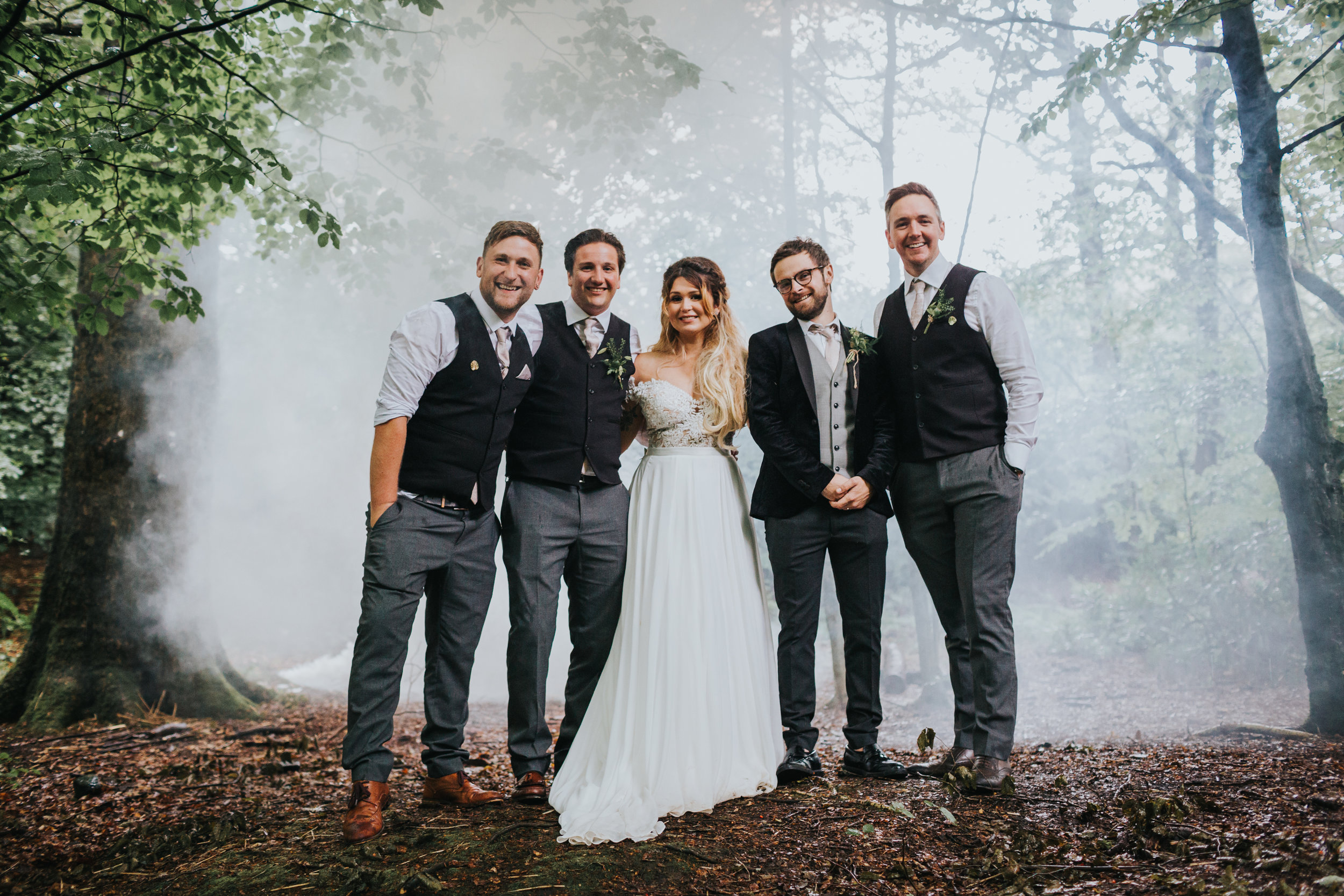 Bride and groom stand with grooms men in front of mist.
