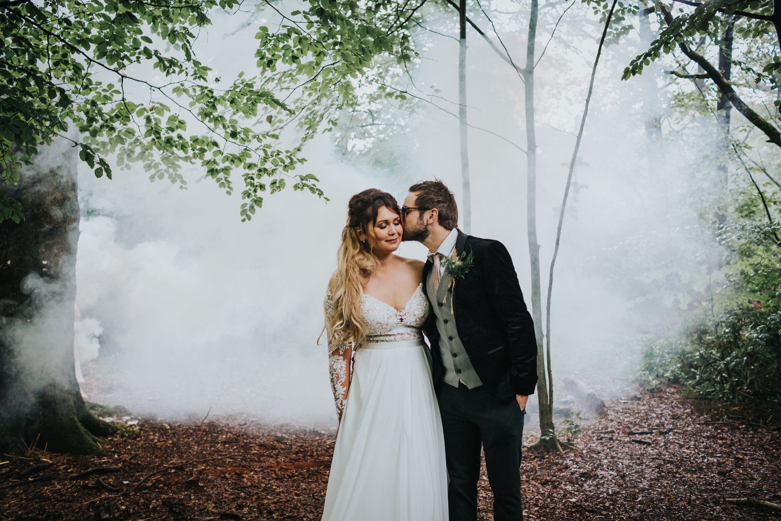 Bride and groom stand together in front of the wood land mist. 