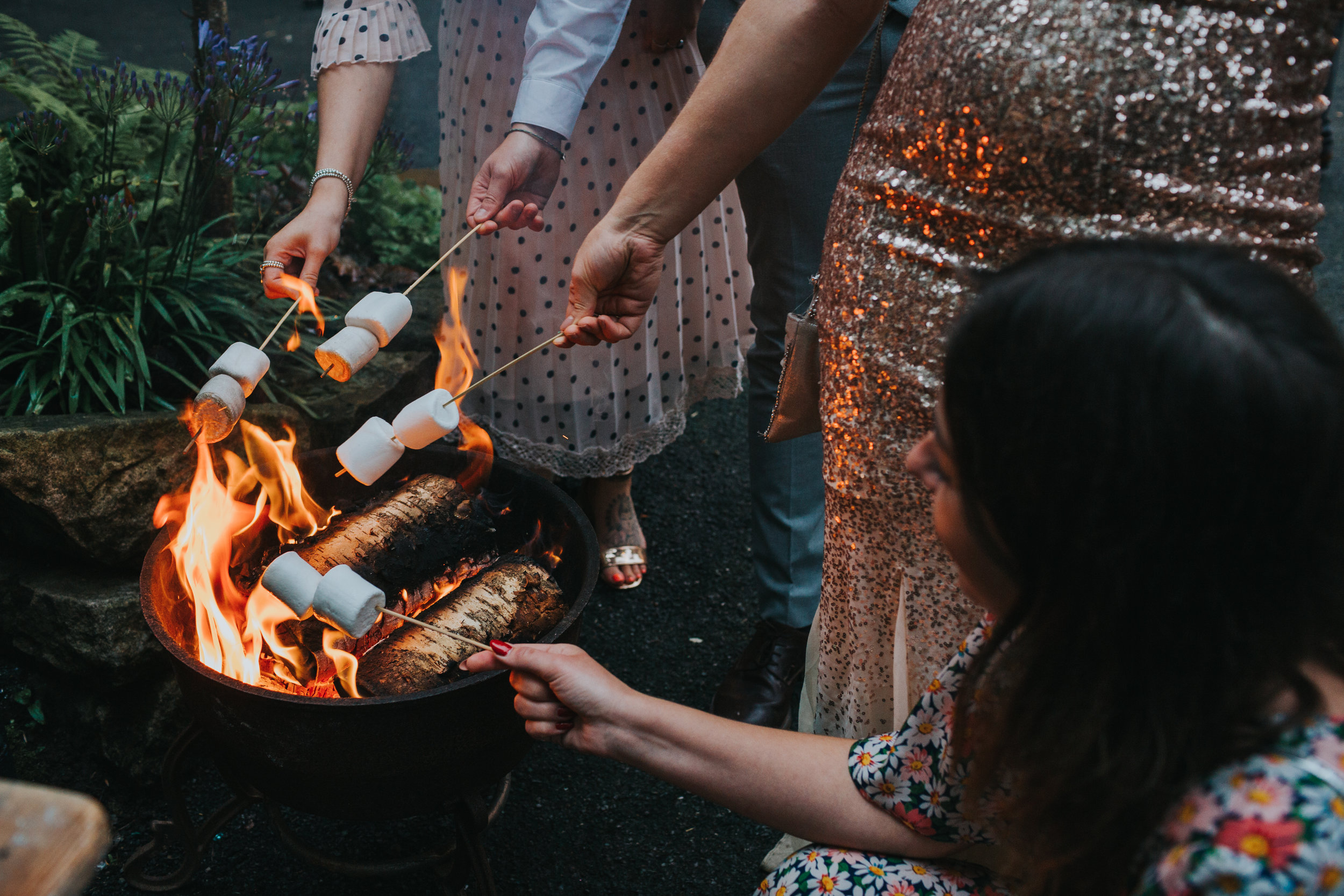 wedding guests cook marsh mellows on the camp fire. 