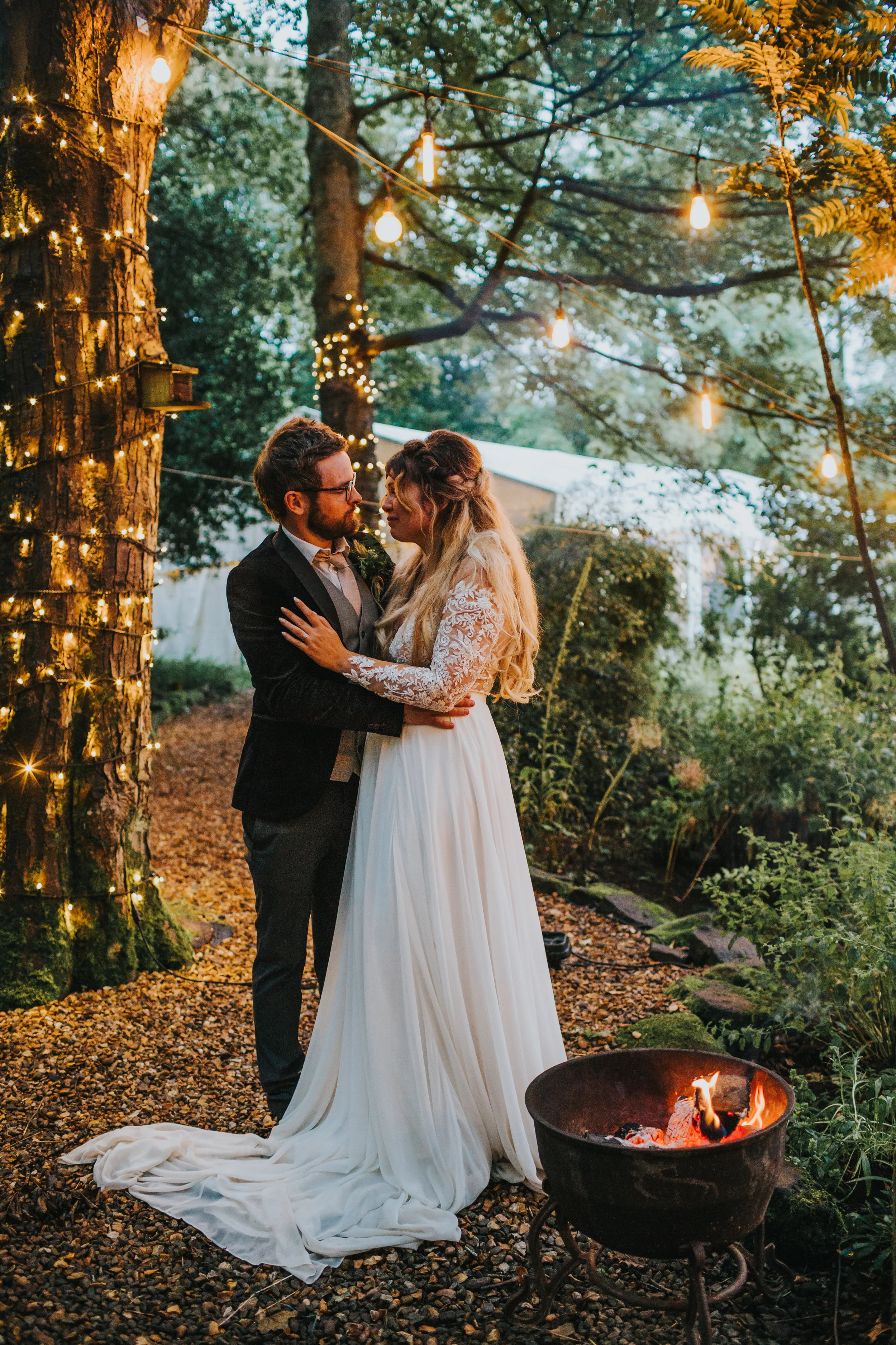 The bride and groom have a cuddle by the camp fire. 
