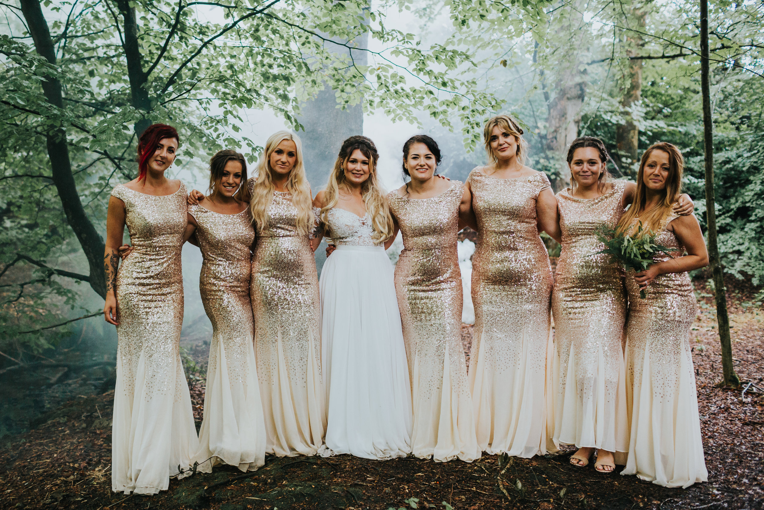 Bridesmaids stand for a photo in the woods with mist behind them. 
