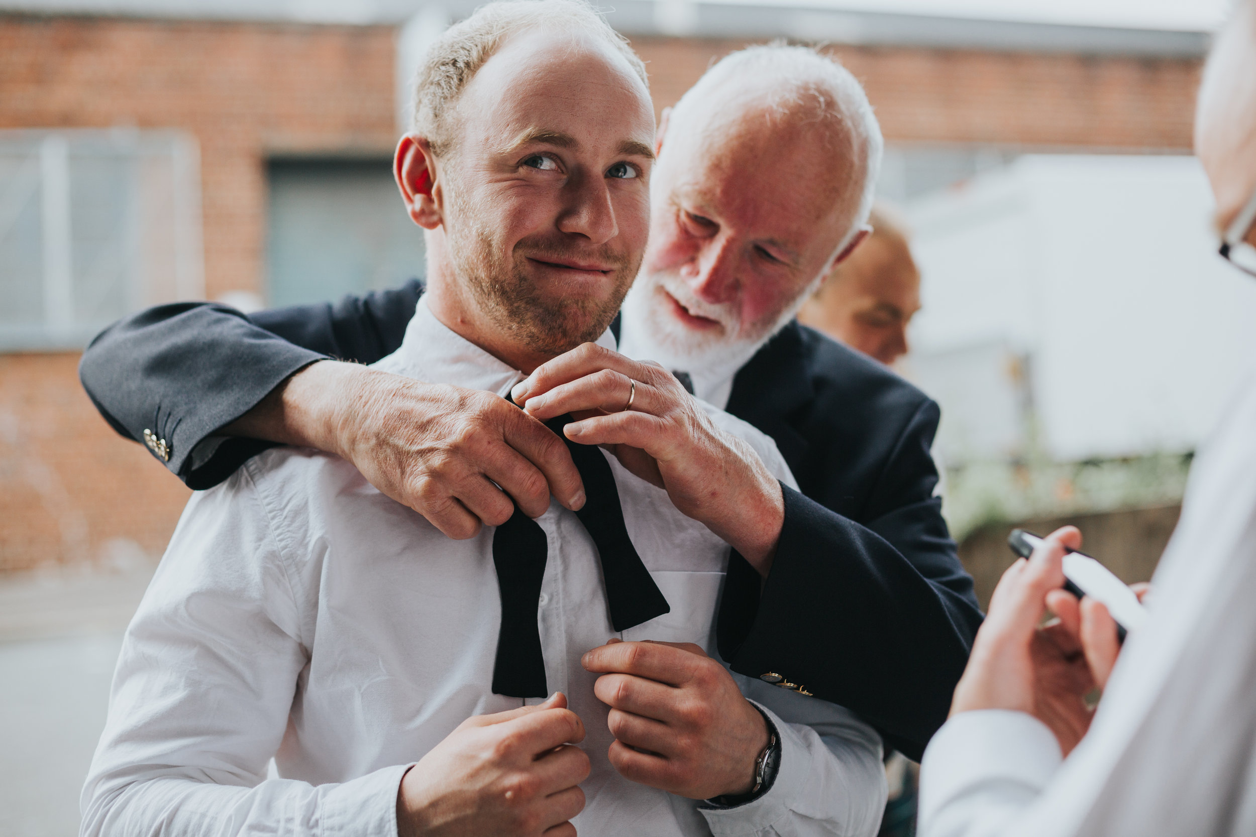 Male wedding guests has his tie fixed by another male wedding guest. 