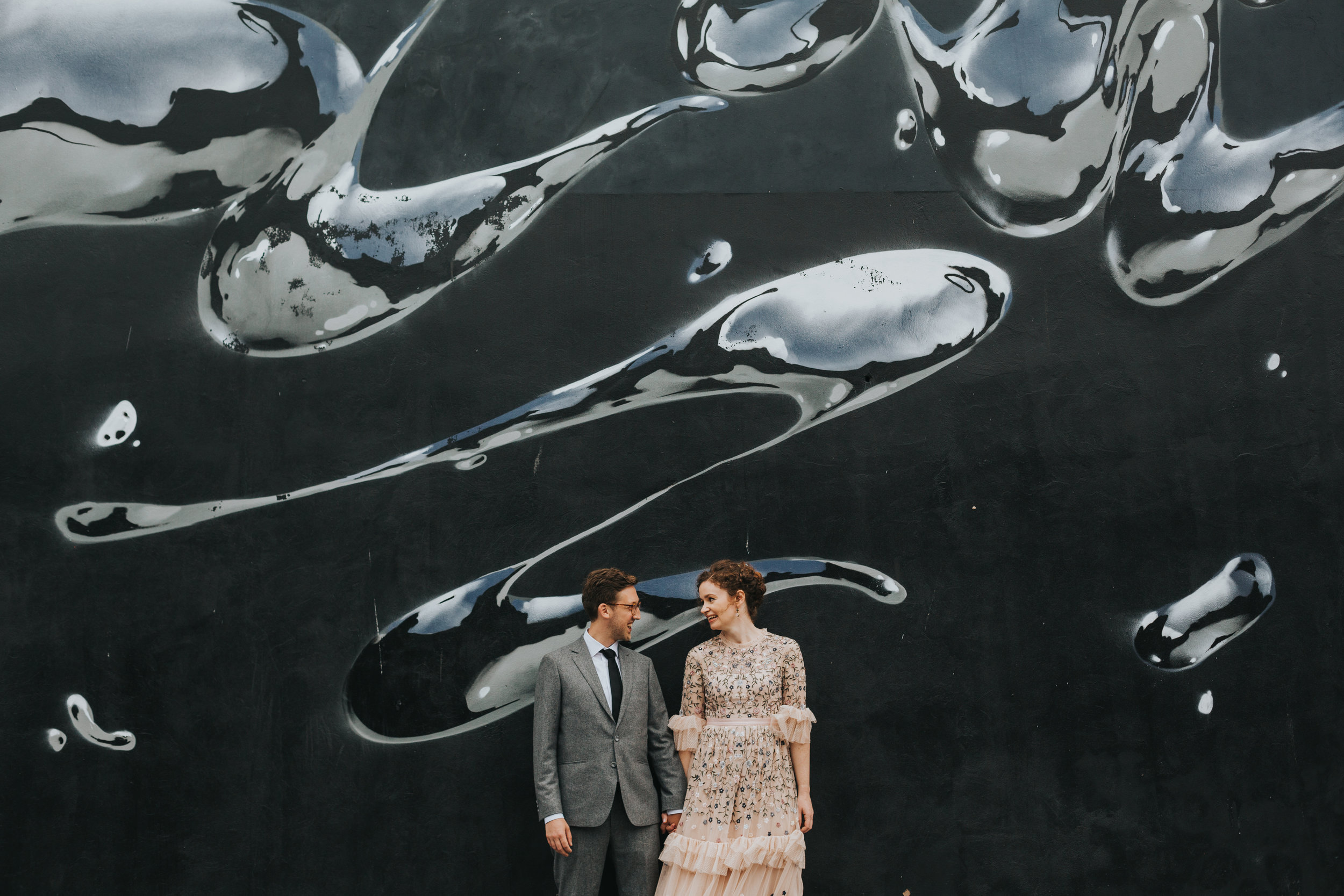 Bride and Groom in front of black and sliver metallic liquid mural. 