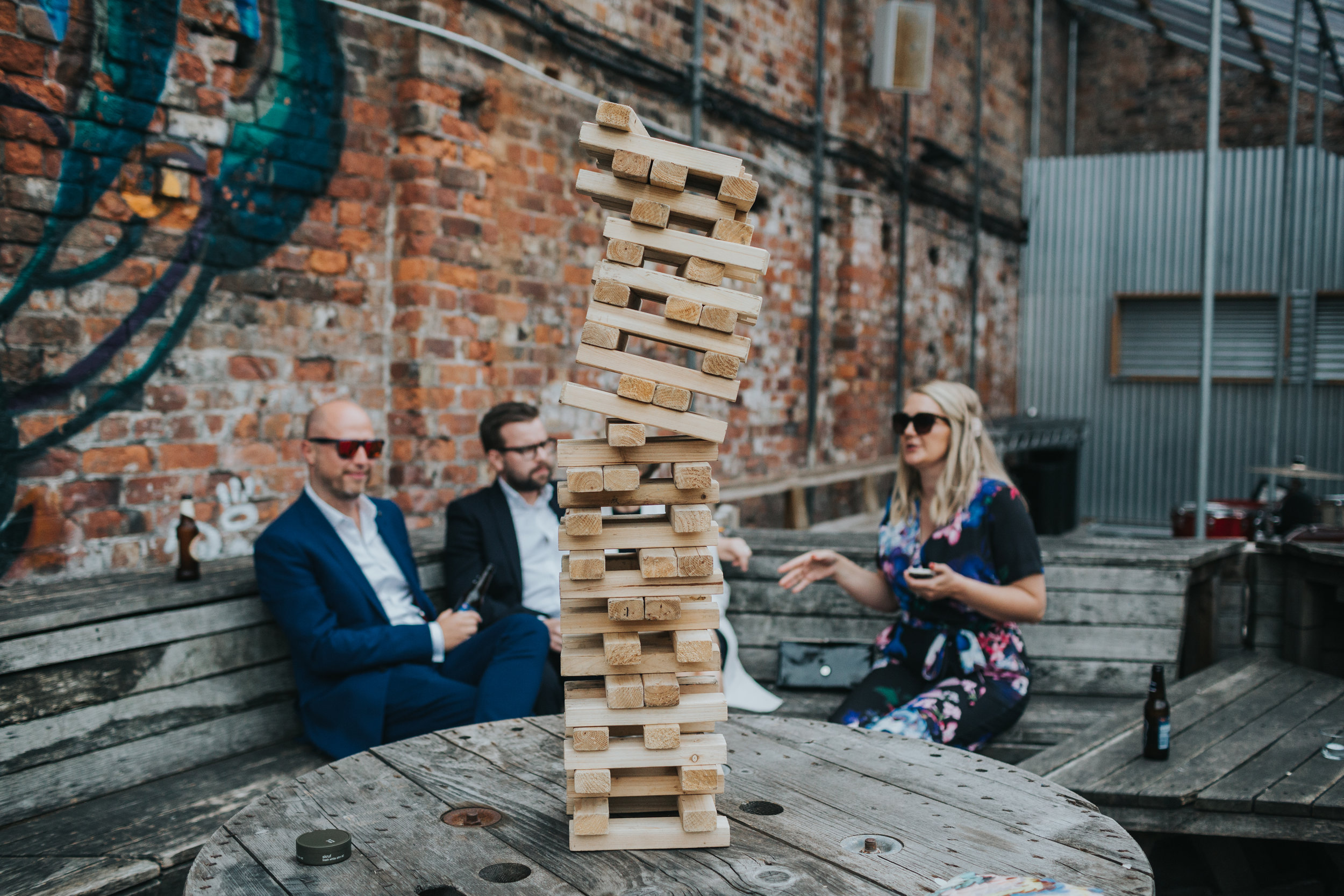 Guests sit nervously next to a precariously stacked Jenga tower. 