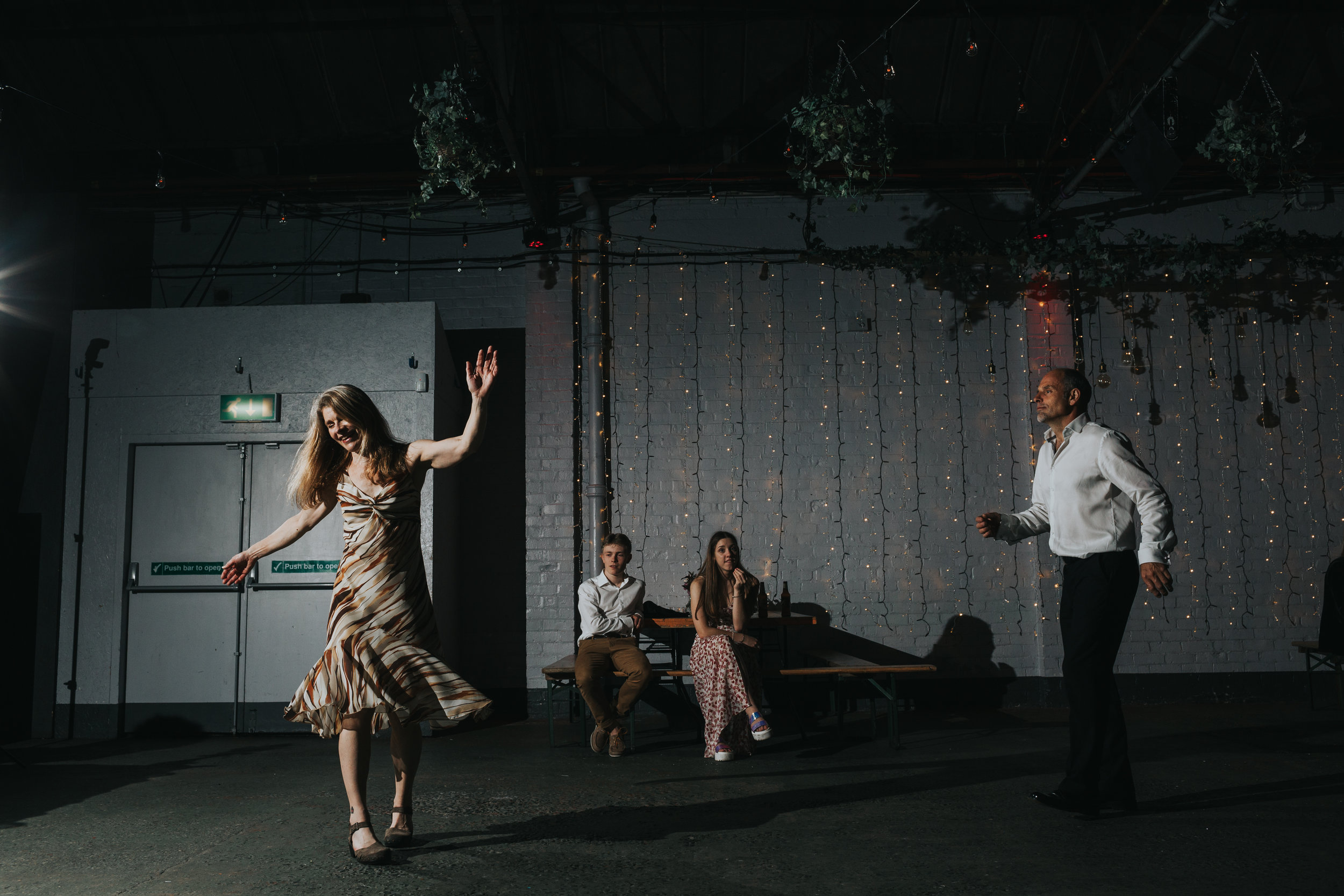 Parents dance joyfully to industrial dance music as children look on bemused.
