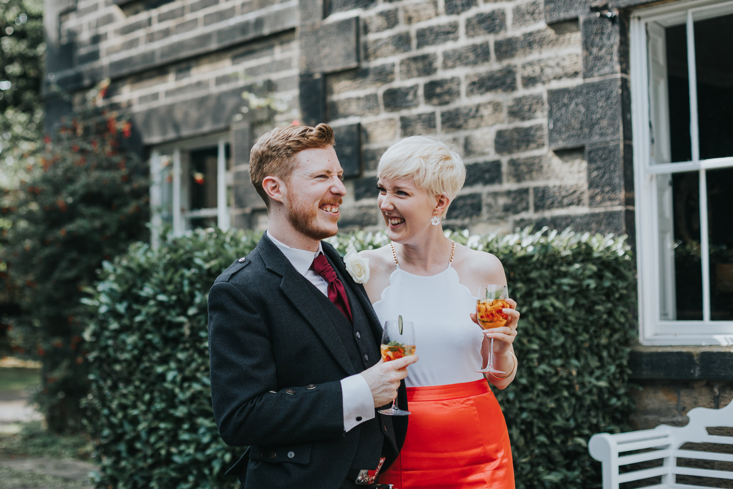 Bride and groom share a laugh and a drink together outside. 